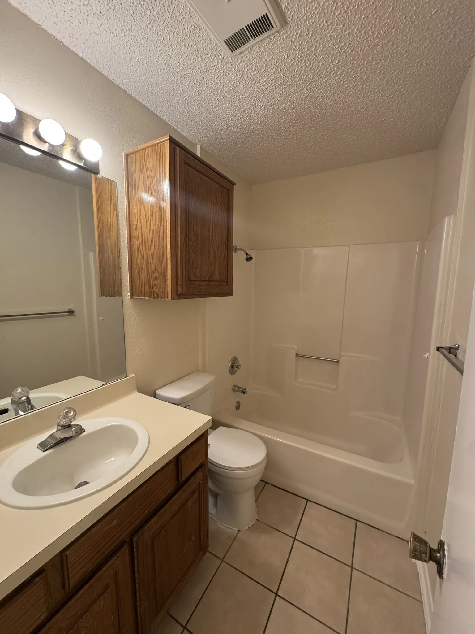 Vanity with integrated sink, wood-finish cabinetry, tile flooring, and a bathtub with shower surround