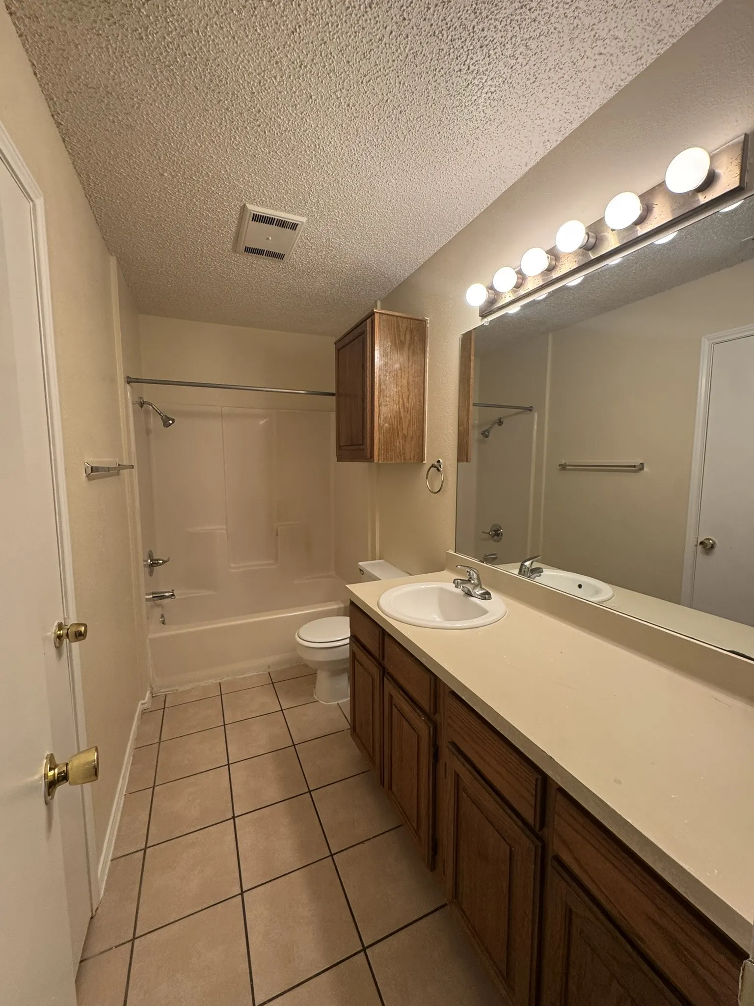 Bathroom featuring a wood-finish vanity with an integrated sink, a full-width mirror, tile flooring, and a shower-over-tub combination