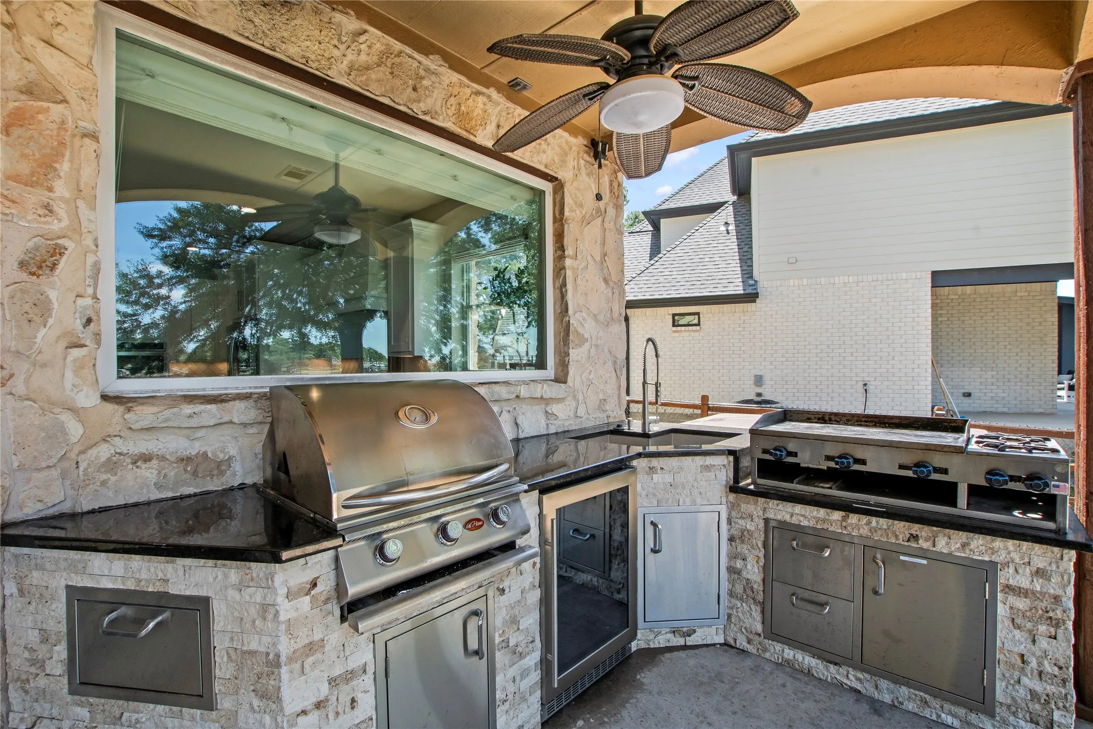 Outdoor kitchen with grill, griddle, sink and beverage refrigerator.