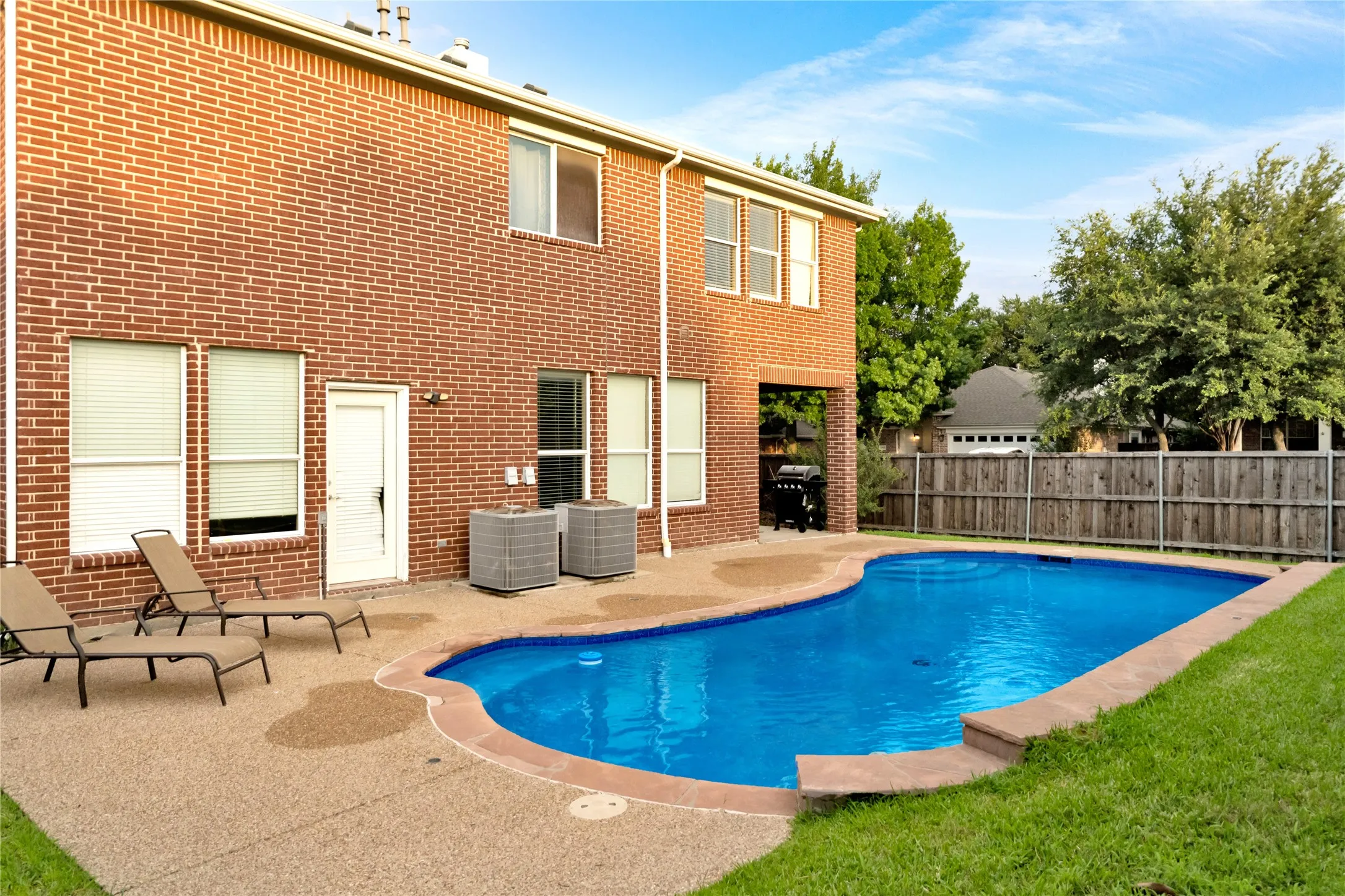 Brick exterior with an in-ground swimming pool, concrete pool surround, and a covered patio area
