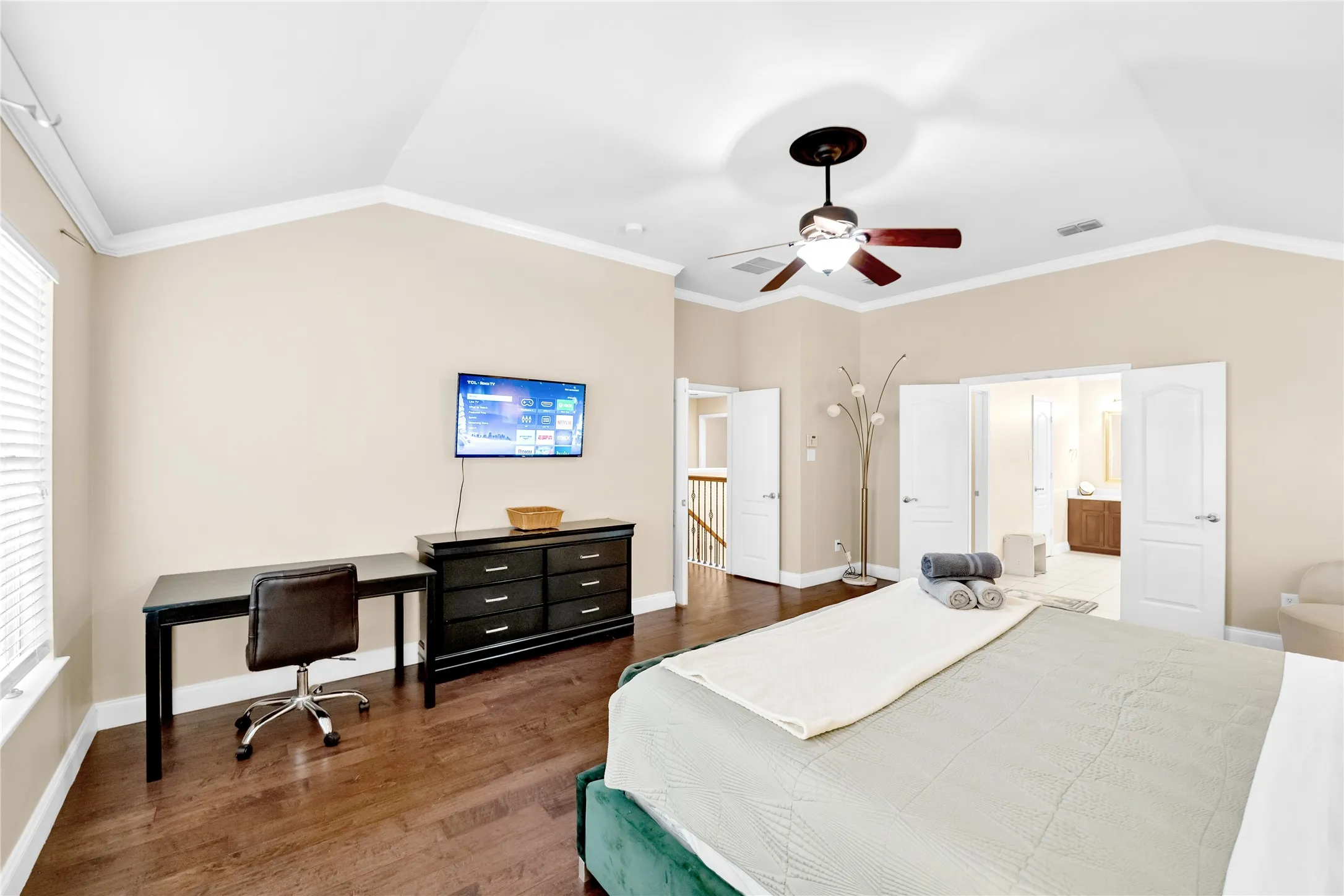 Vaulted ceiling with crown molding, wood-finish flooring, ceiling fan with light fixture, and double doors to additional space