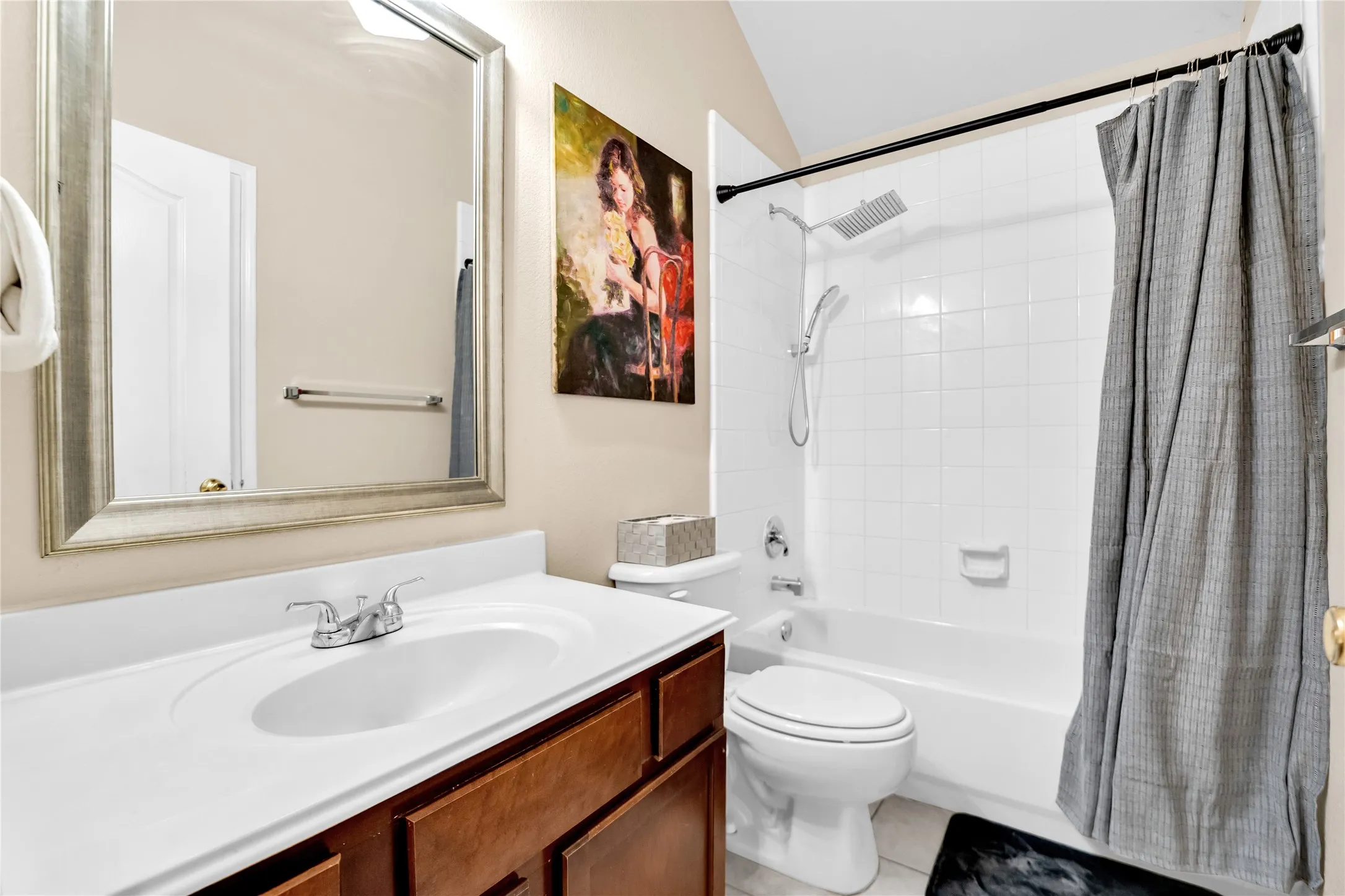 Bathroom featuring a white vanity top, wood-finish cabinetry, a rectangular framed mirror, a shower/tub combination with white subway tile surround, and a rainfall showerhead with an additional handheld sprayer