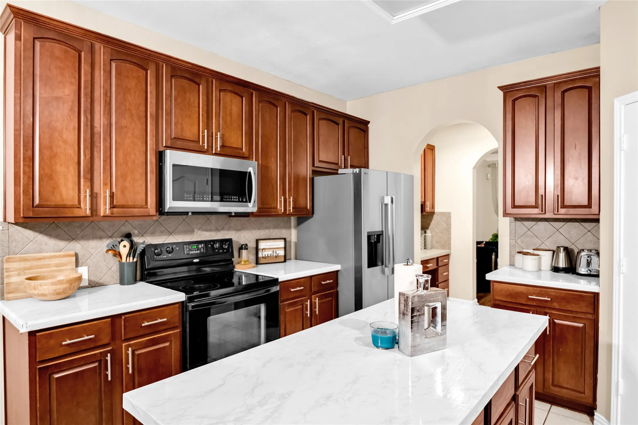 Kitchen featuring wood cabinetry, stainless steel appliances, white countertops, and a neutral tile backsplash