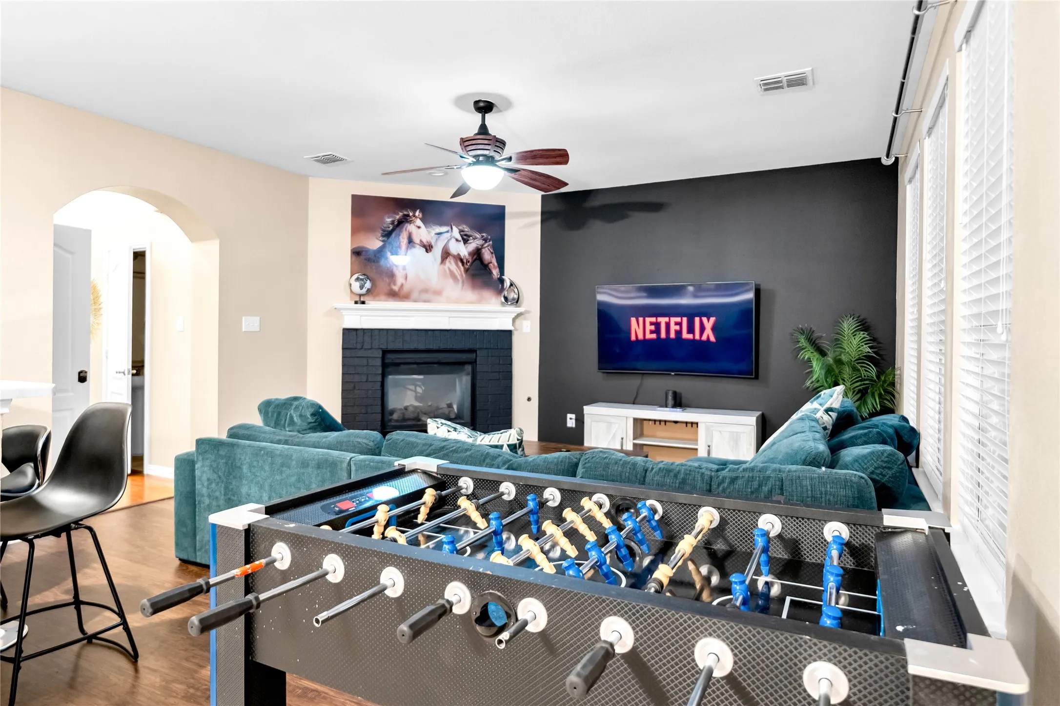 Open-concept living area featuring wood-finish flooring, a black brick fireplace, and a ceiling fan
