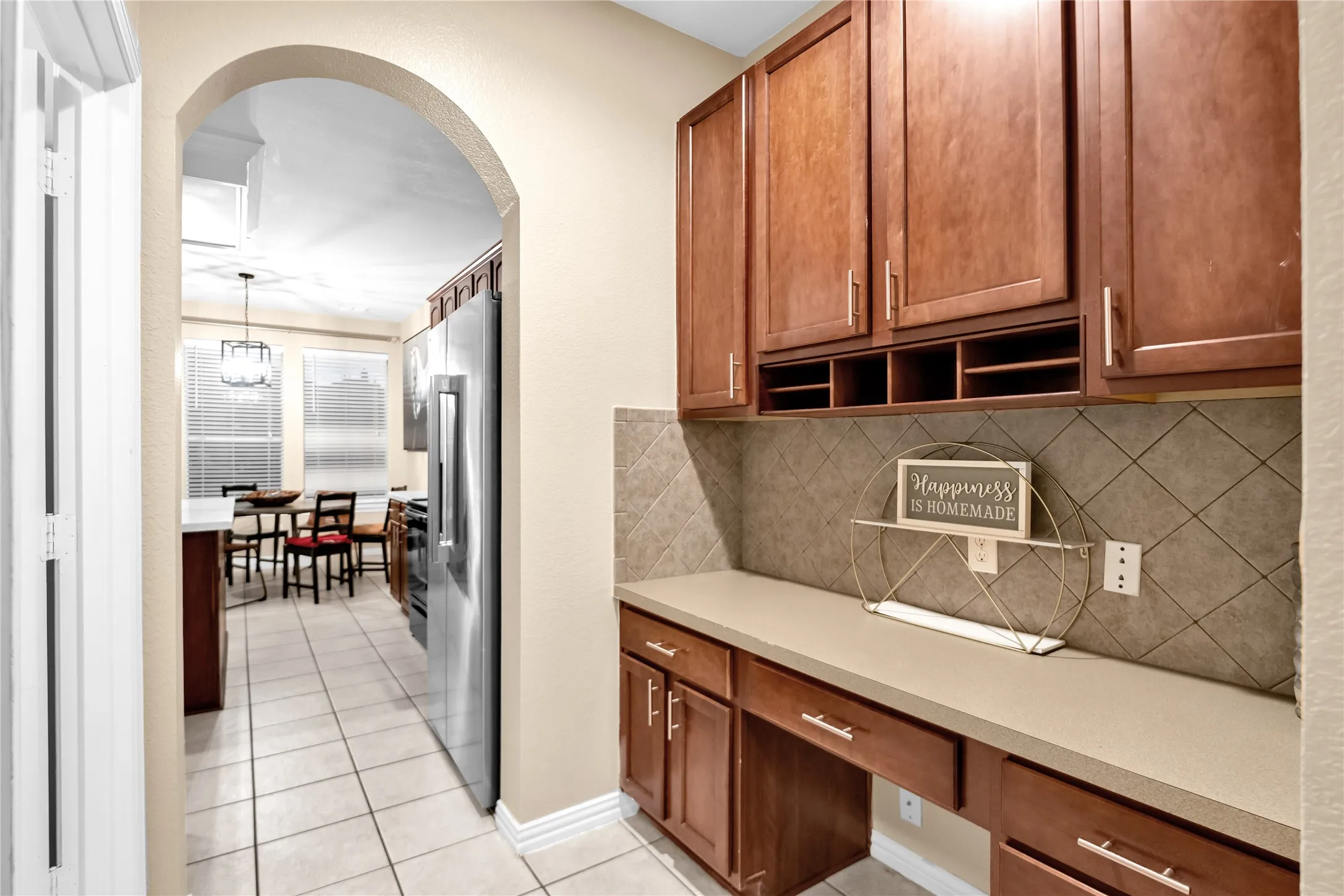 Archway entry leading to a kitchen with tile flooring, a large stainless steel refrigerator, and ample natural light from multiple windows