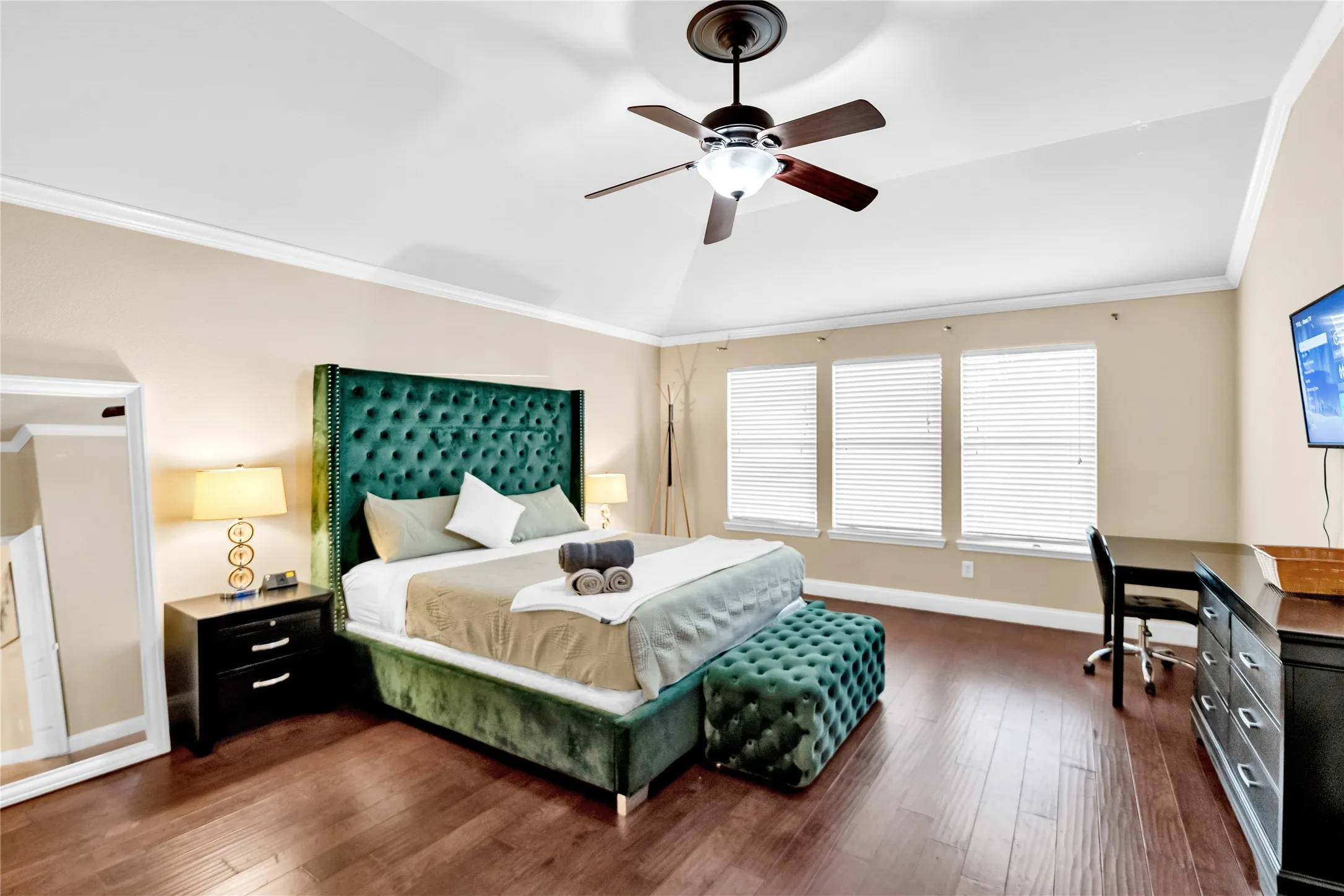 Vaulted ceiling with a ceiling fan, crown molding, three windows, and wood-finish flooring