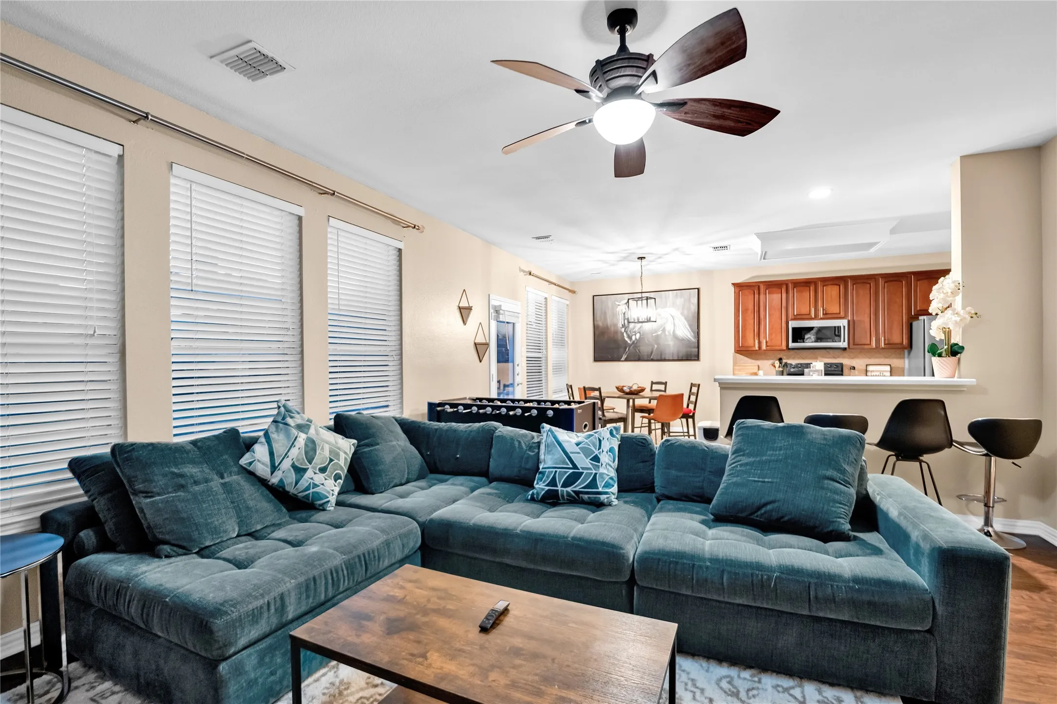 Living area with wood-finish flooring, three windows with blinds, and a ceiling fan