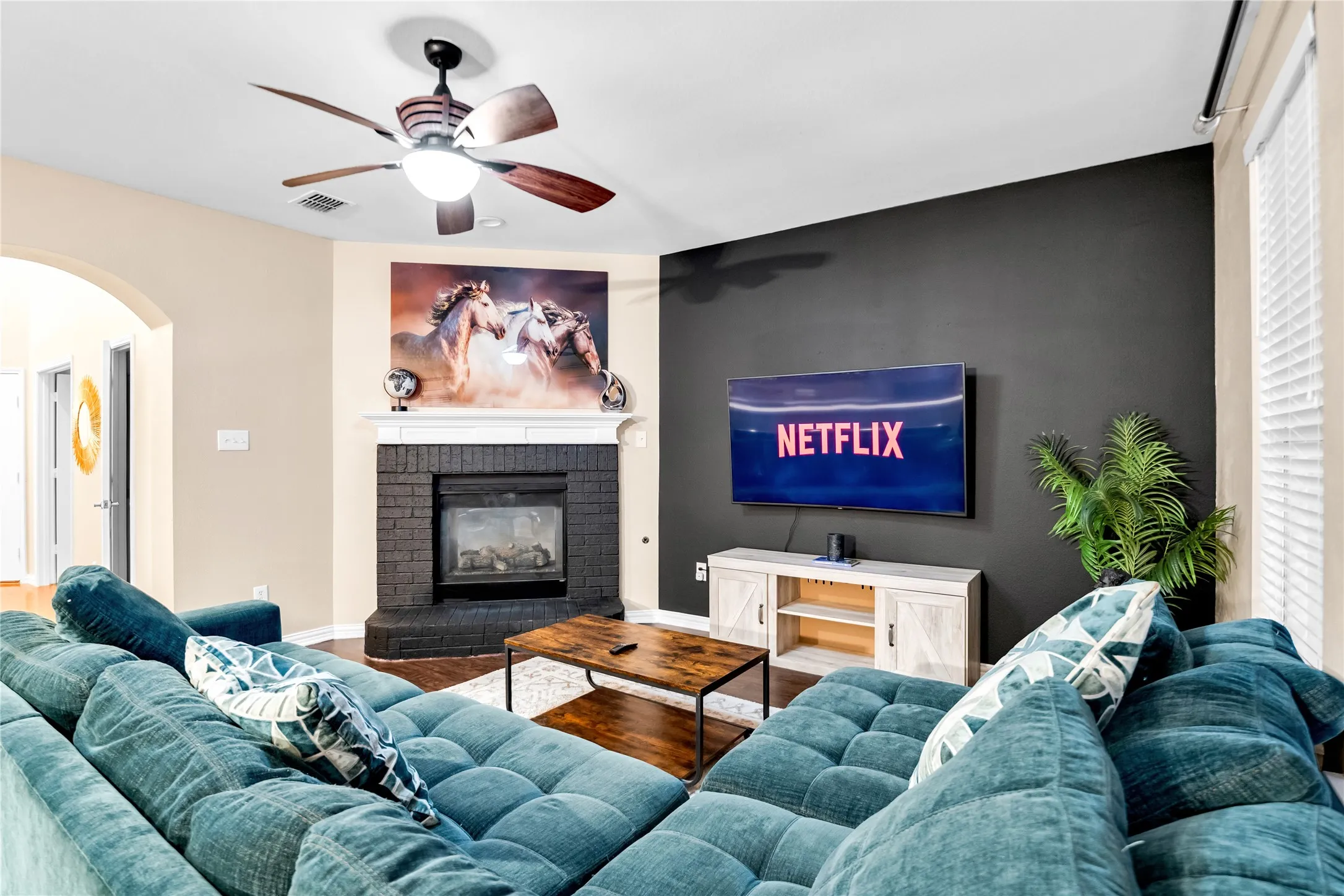 Living area featuring a ceiling fan, fireplace with a white mantel, and arched doorway