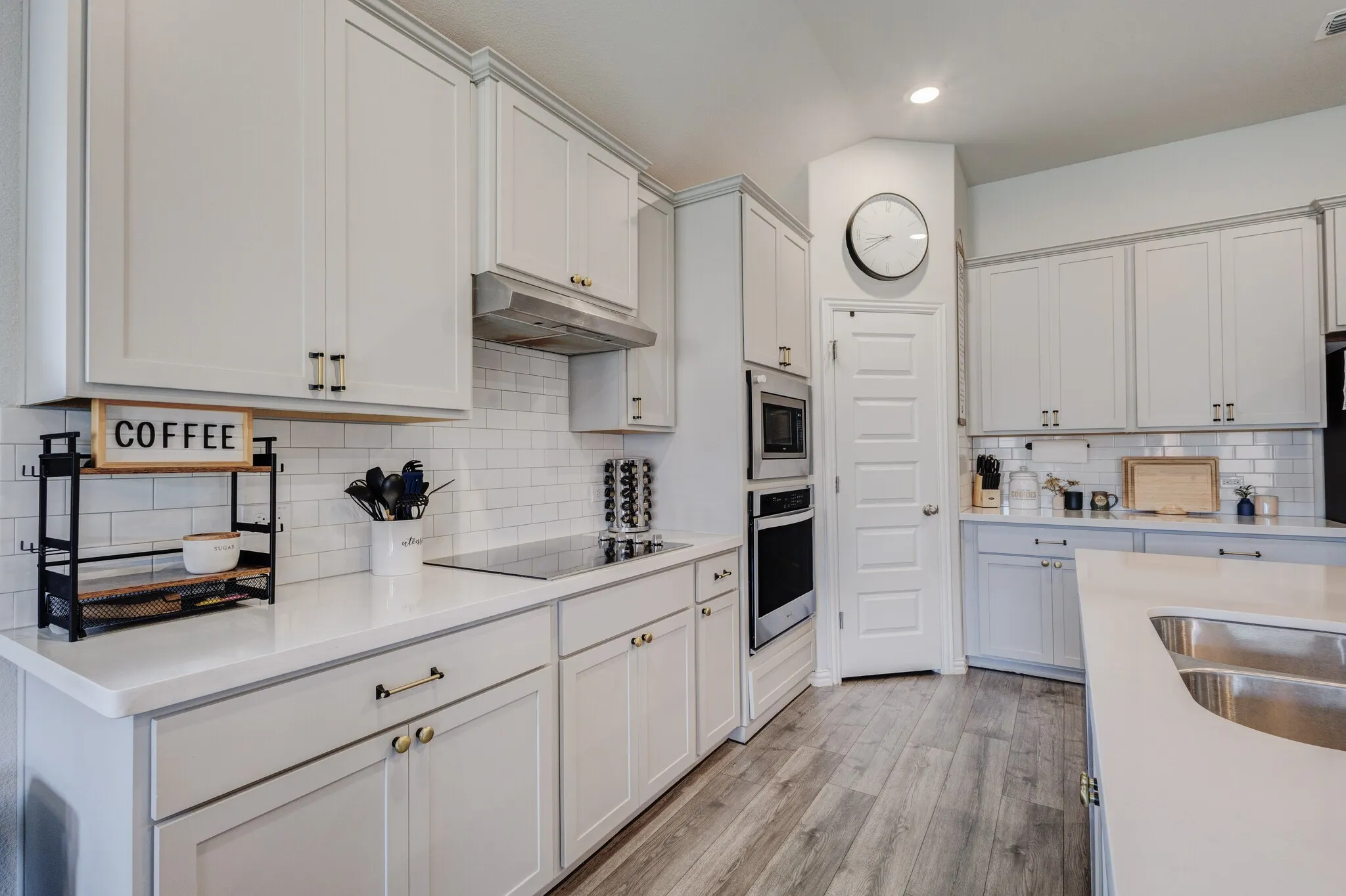 White shaker cabinetry, subway tile backsplash, built-in stainless steel appliances, wood-finish flooring, and a kitchen island with an undermount double sink
