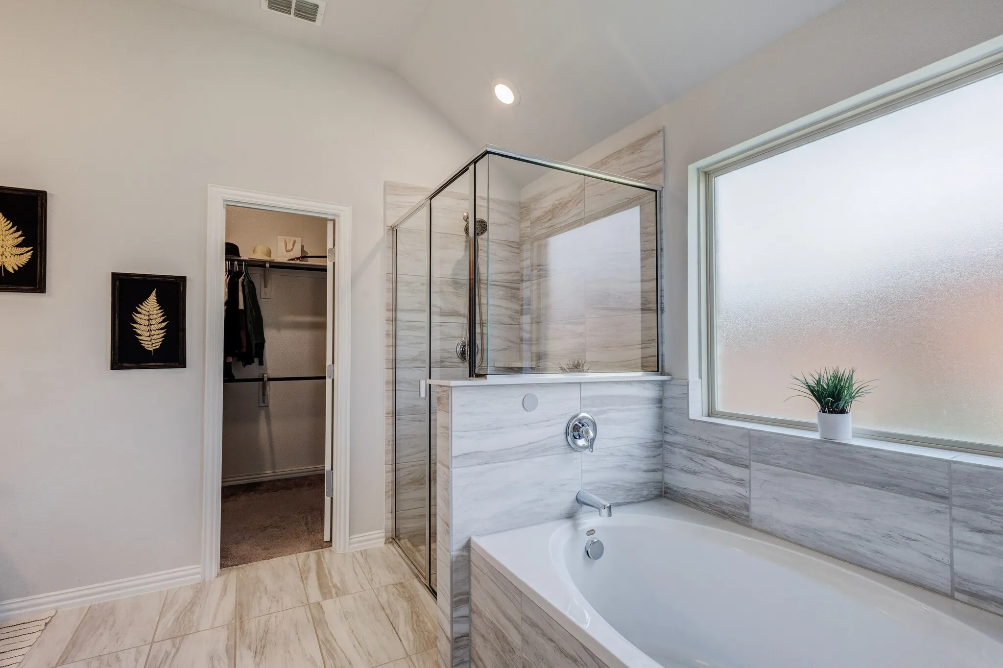 Soaking tub with chrome fixtures, glass-enclosed shower, light-toned wall tile, and a frosted window