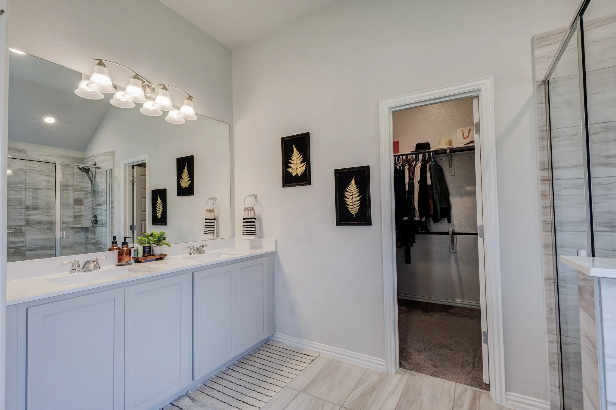 Dual vanity with undermount sinks, an expansive wall mirror, a built-in shower with glass enclosure, a dedicated walk-in closet, and light wood-finish flooring