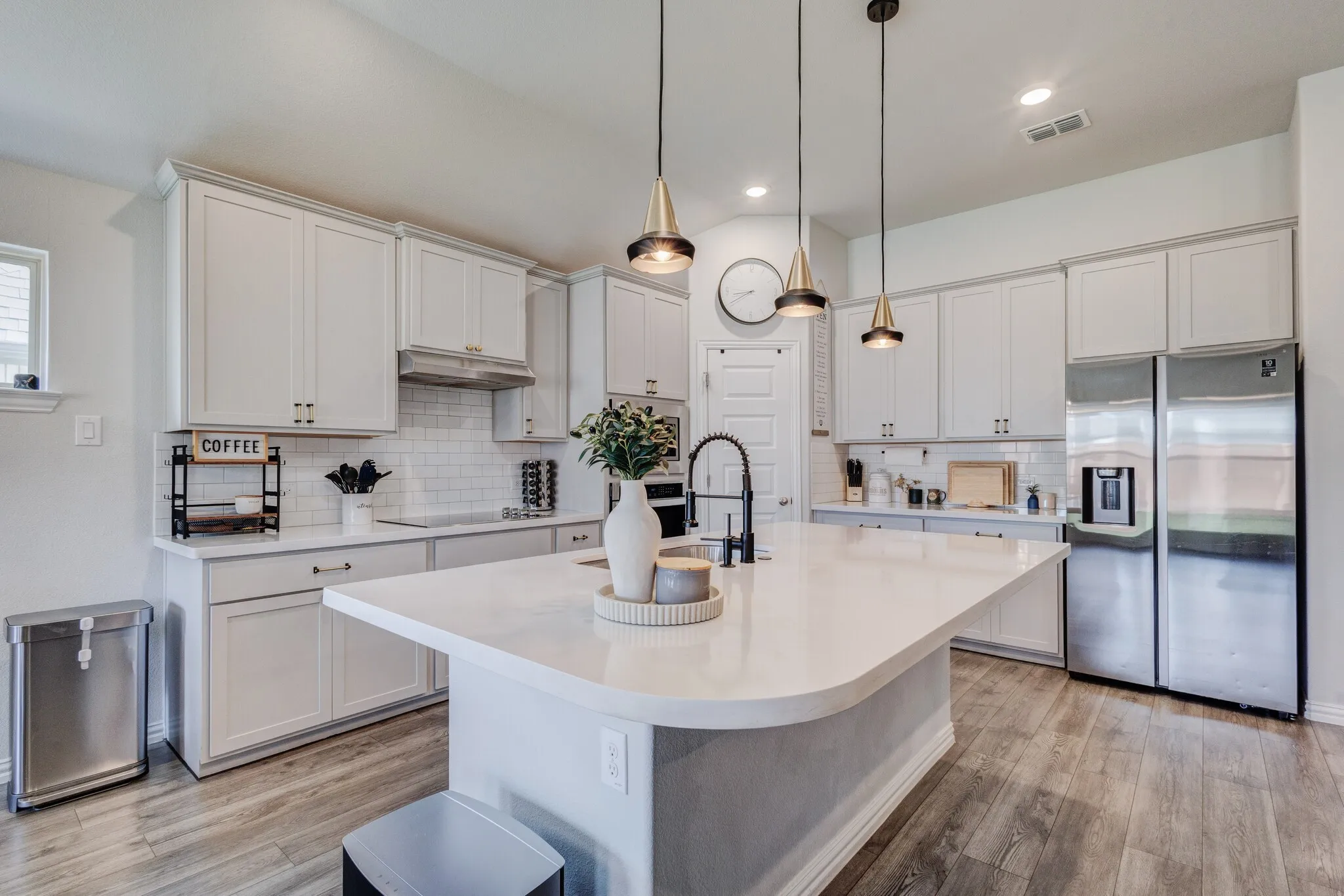 Kitchen featuring an expansive island with a white countertop, white shaker cabinetry, stainless steel appliances, and wood-finish flooring