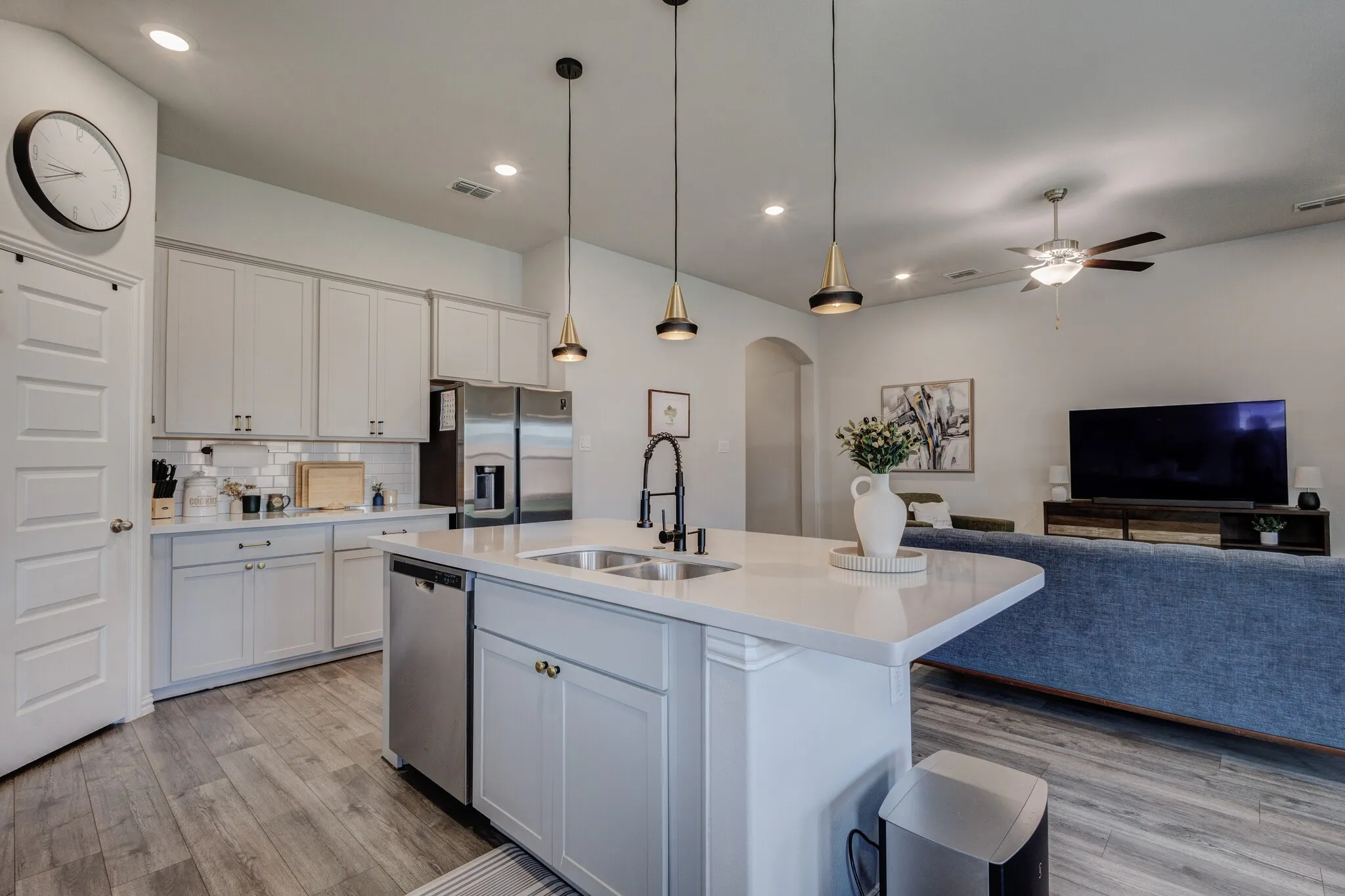 Kitchen island with an undermount sink, pendant lighting, stainless steel dishwasher, and light-toned cabinetry