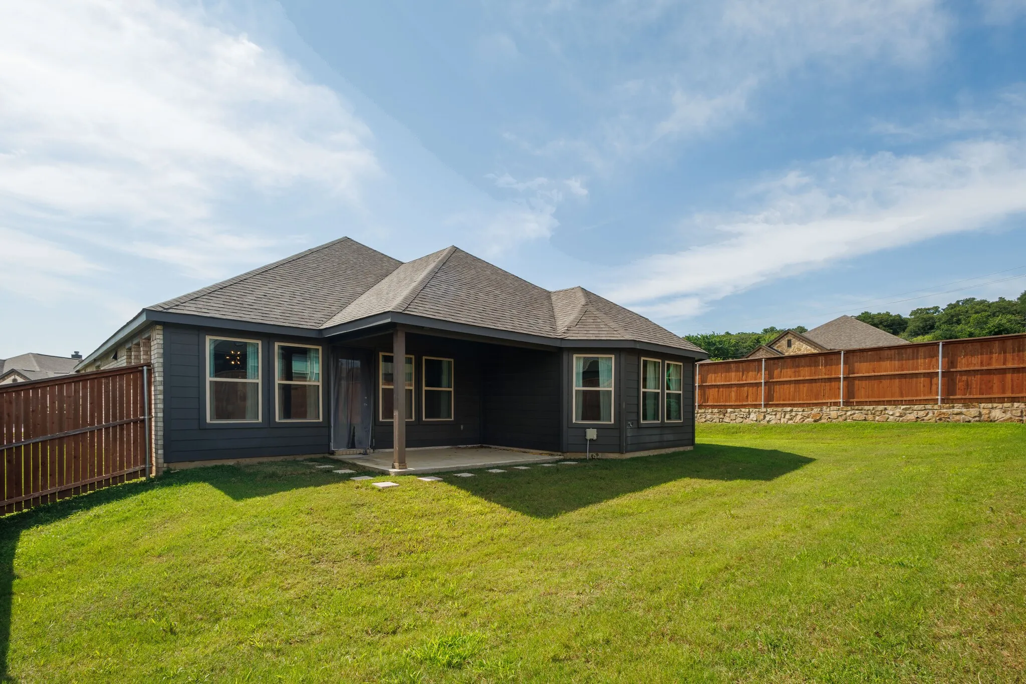 Expansive backyard featuring a covered patio, wood fencing, and stone retaining wall
