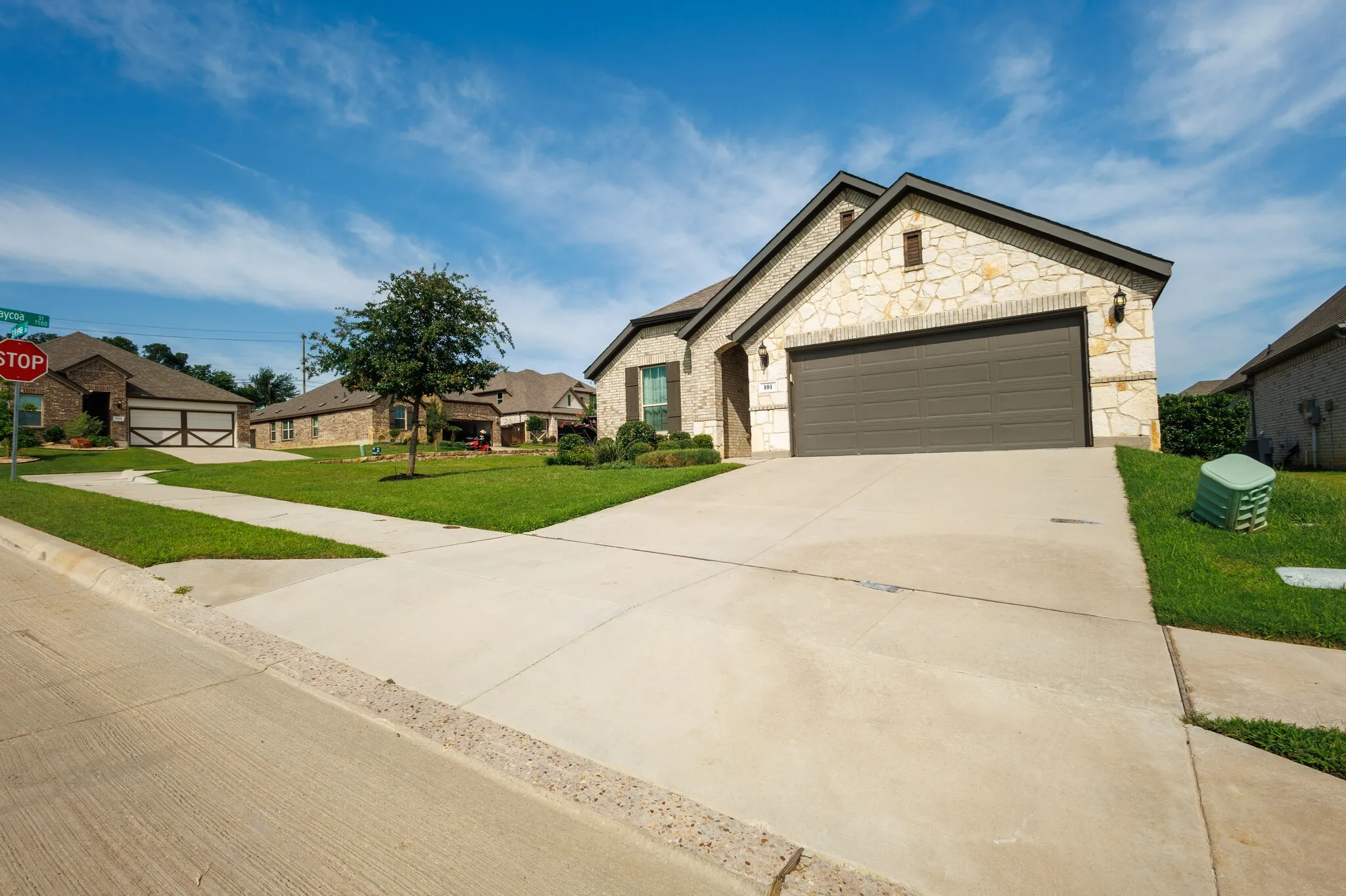 Stone exterior, concrete driveway, attached garage, gabled roofline, manicured lawn