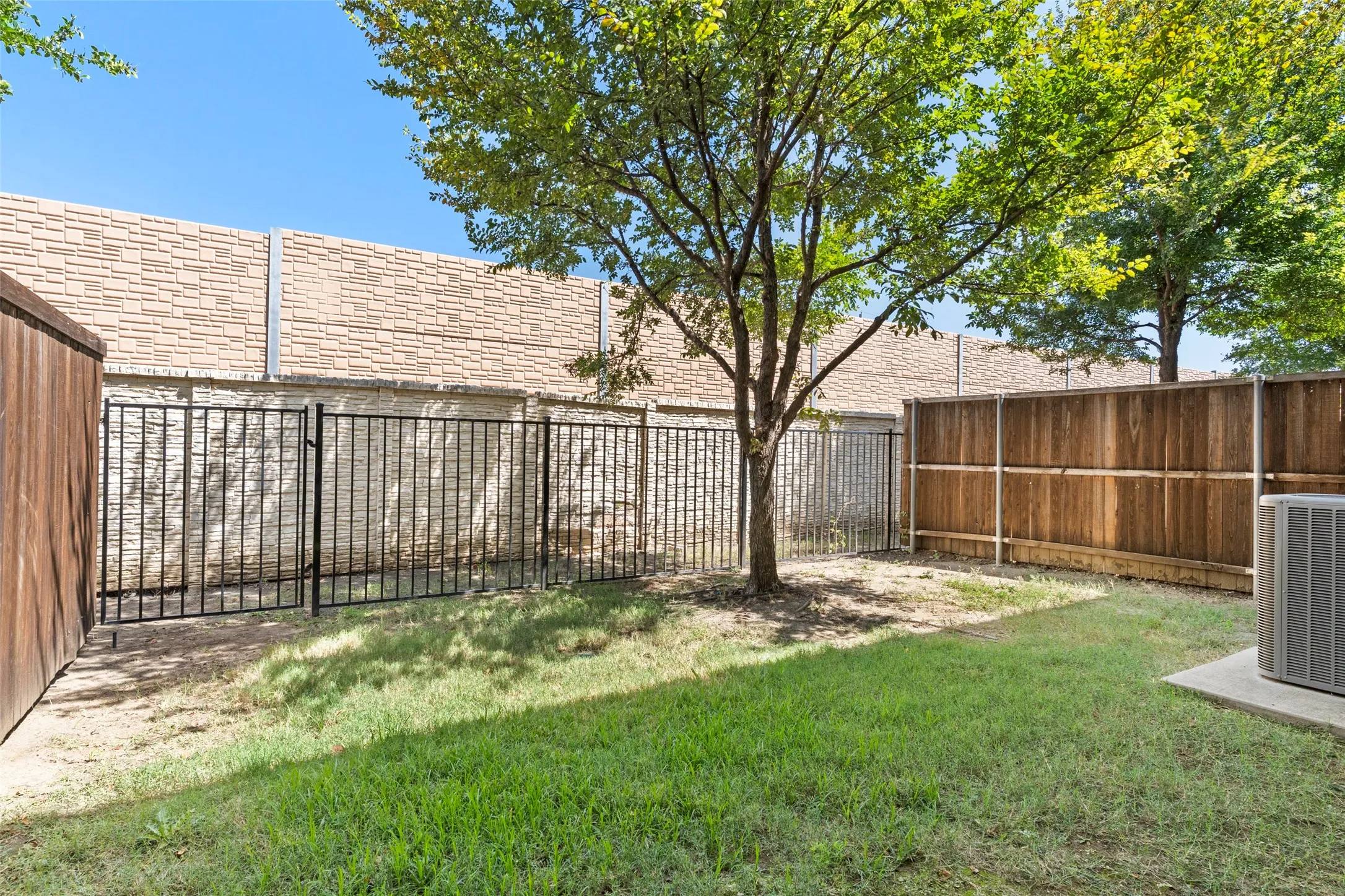 Fenced backyard featuring a manicured lawn, established tree, and stone wall backdrop