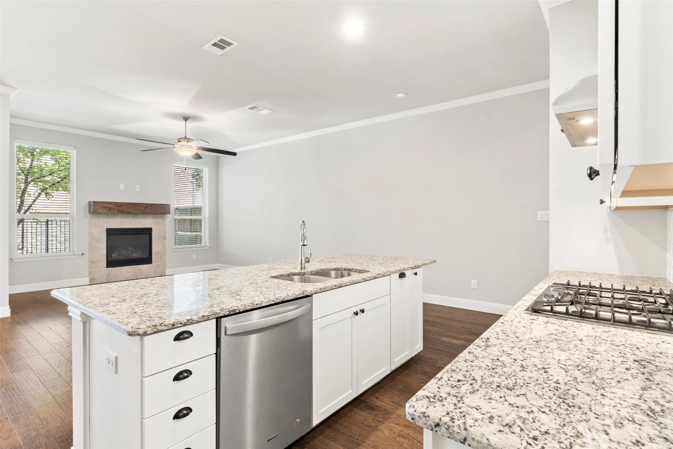 Gourmet kitchen featuring white cabinetry, granite countertops, a large island with prep sink, stainless steel appliances including a gas cooktop and dishwasher, and wood-finish flooring throughout