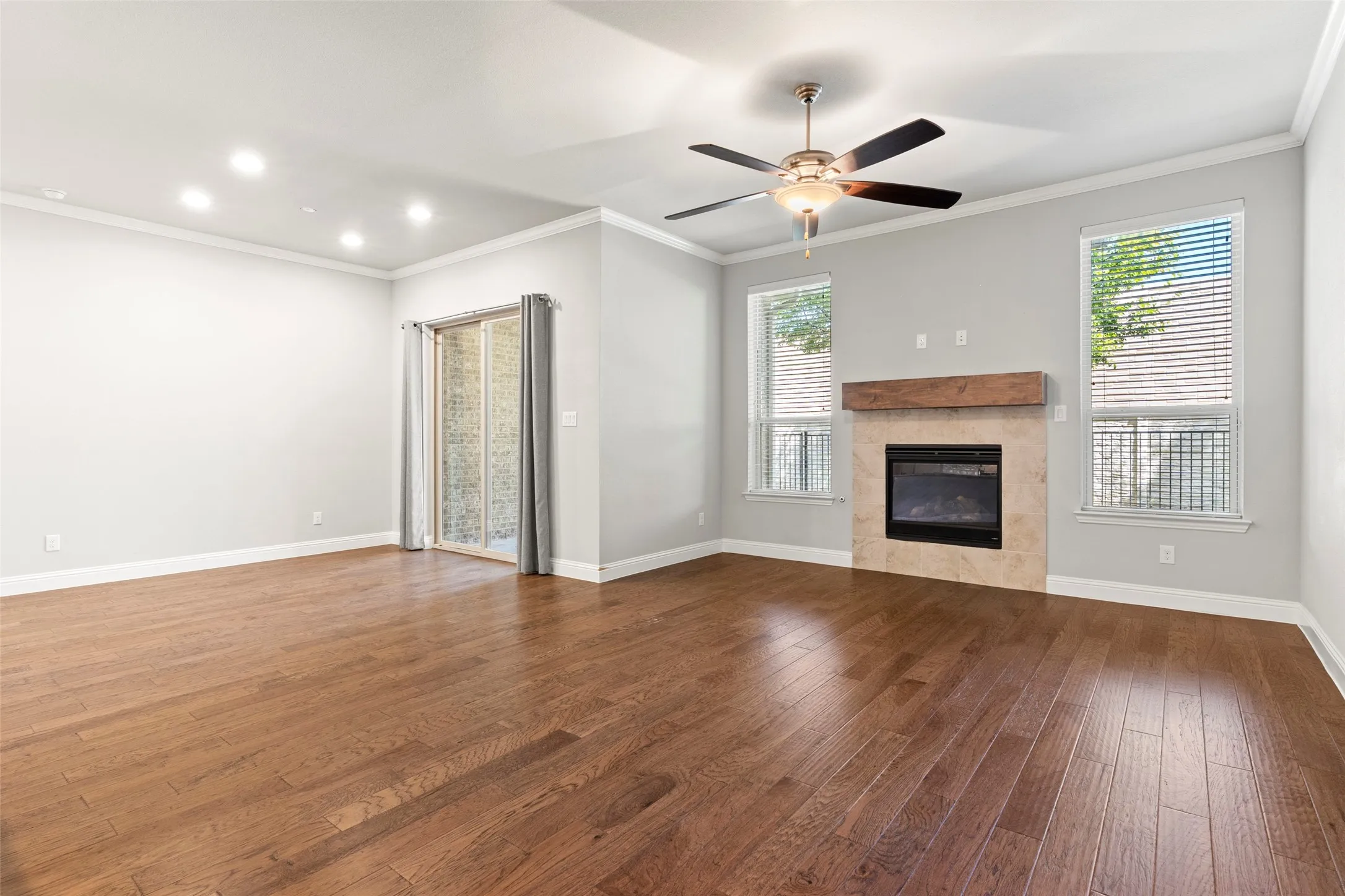 Spacious living room showcasing warm wood-finish flooring, recessed ceiling lighting, and a ceiling fan with brushed metal accents