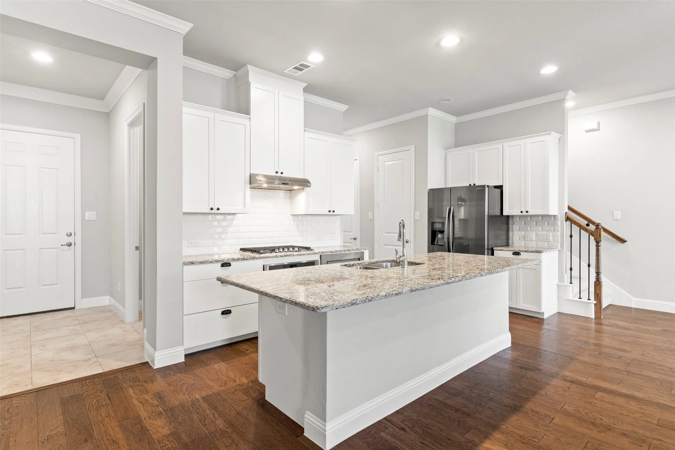 Chef's kitchen featuring white cabinetry, granite countertops, a large center island with breakfast bar seating, stainless steel appliances including a gas range and French-door refrigerator, subway tile backsplash, recessed lighting, and hardwood flooring throughout the open concept space