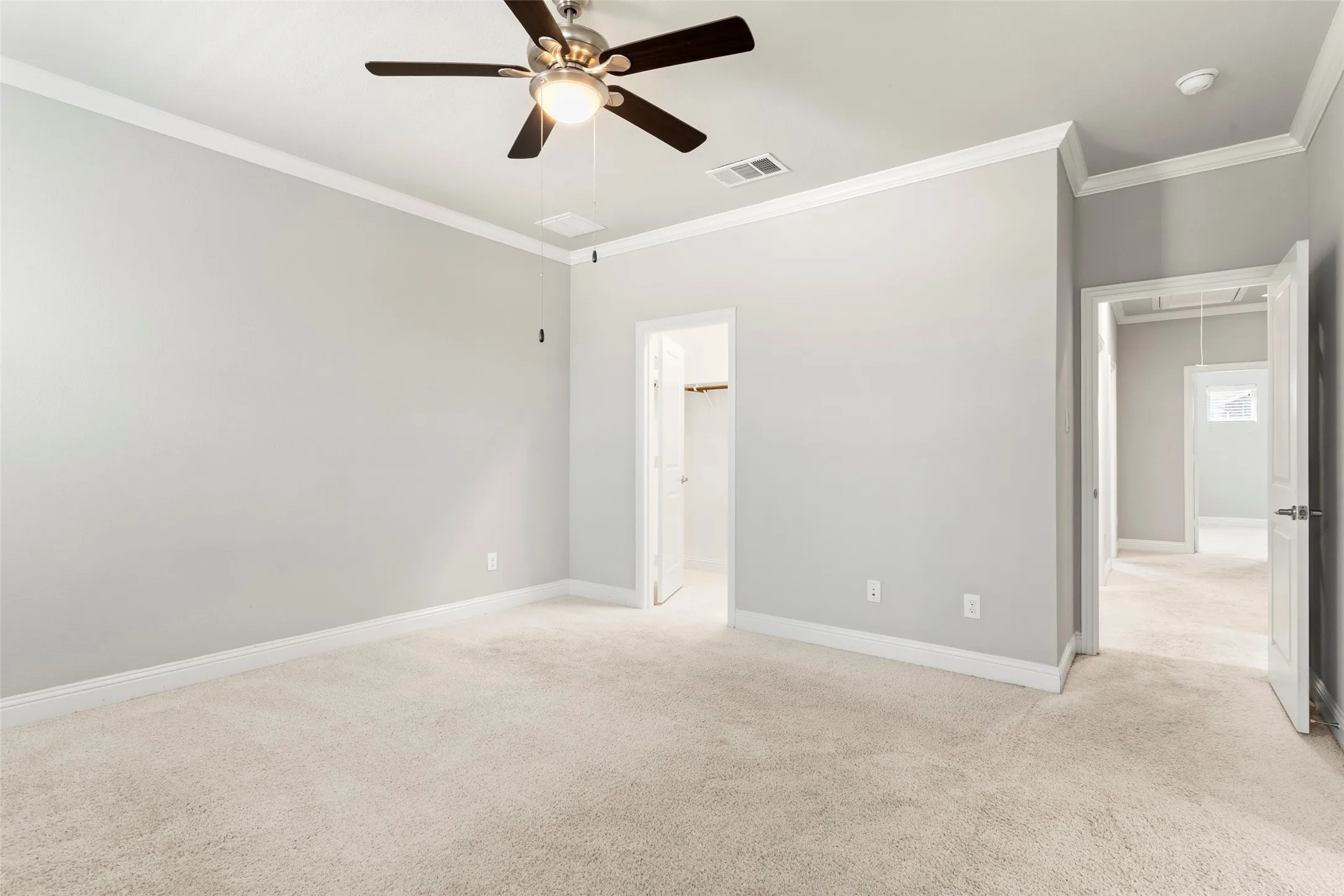Spacious primary bedroom with neutral wall finishes, plush carpet flooring, ceiling fan with integrated lighting, and multiple windows providing natural illumination