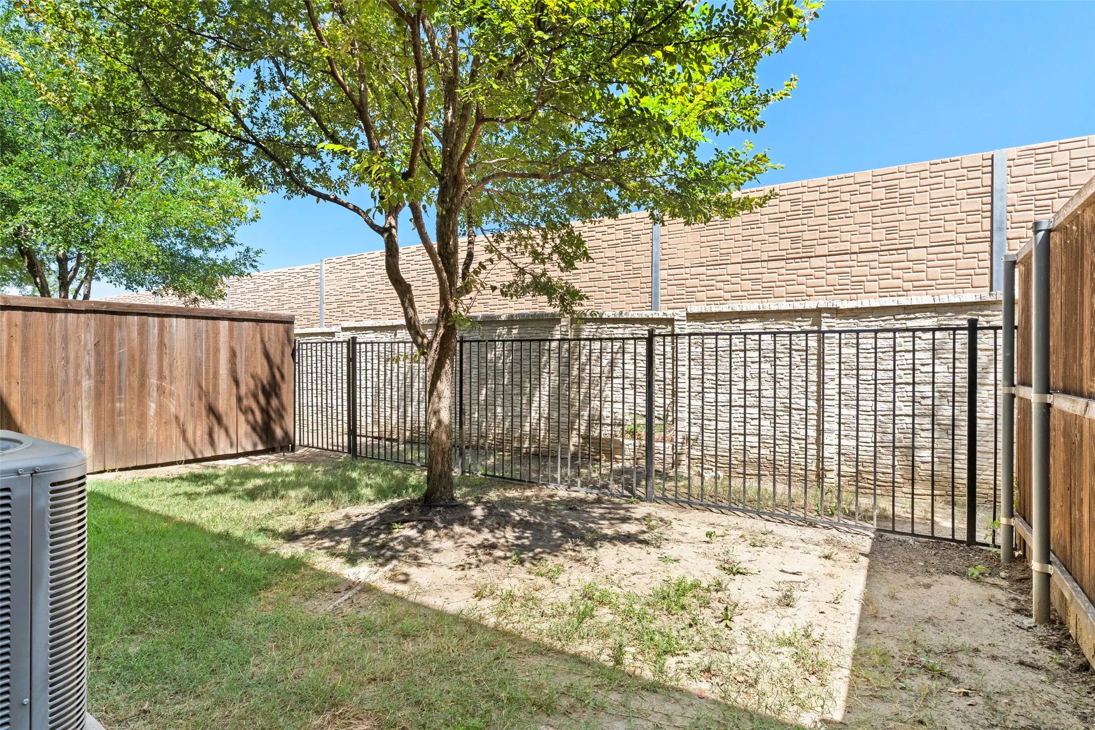 Enclosed backyard featuring a wrought iron fence, wood privacy fence, and a mature tree