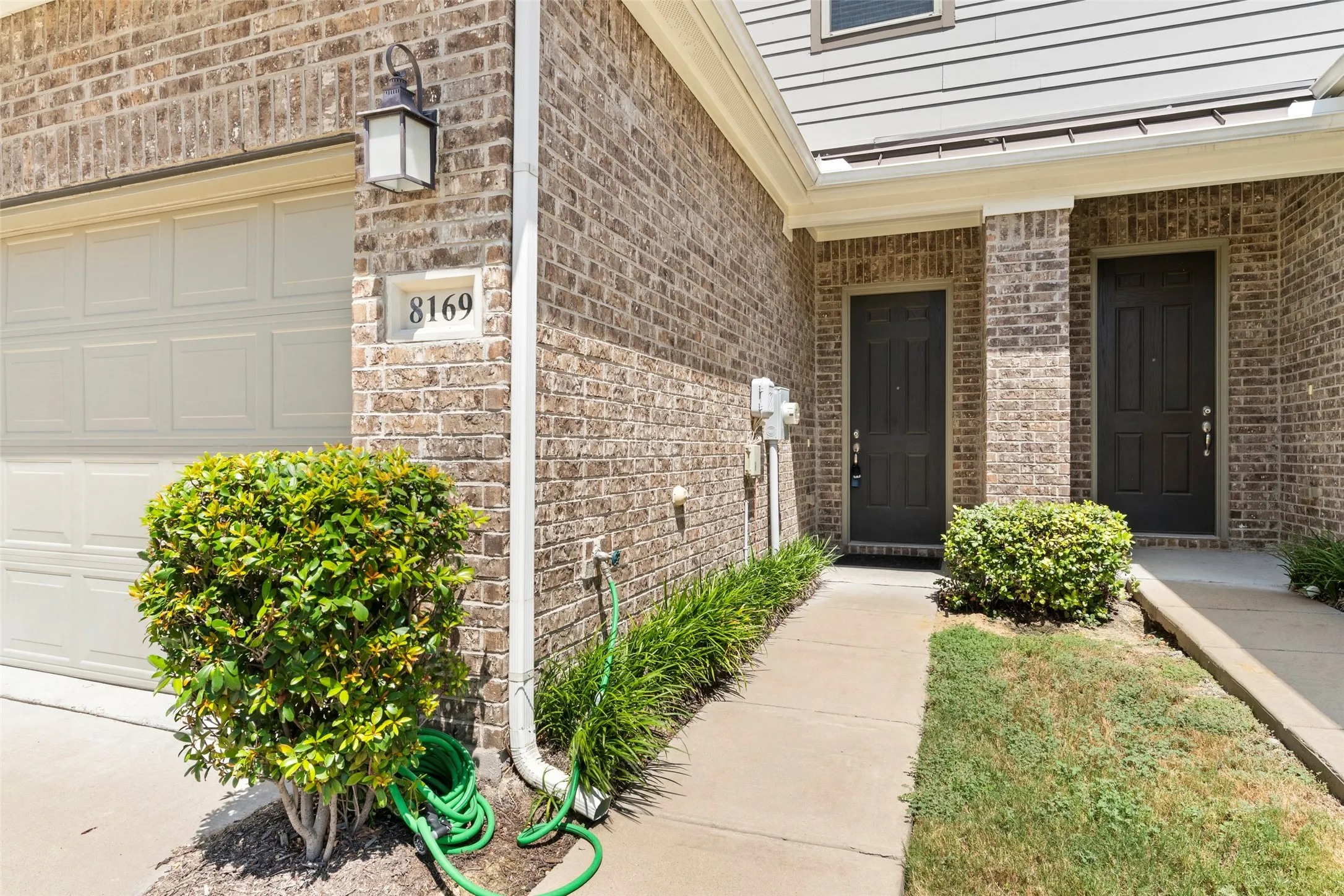 Welcoming brick facade with white garage door, black entry doors, and professional exterior lighting