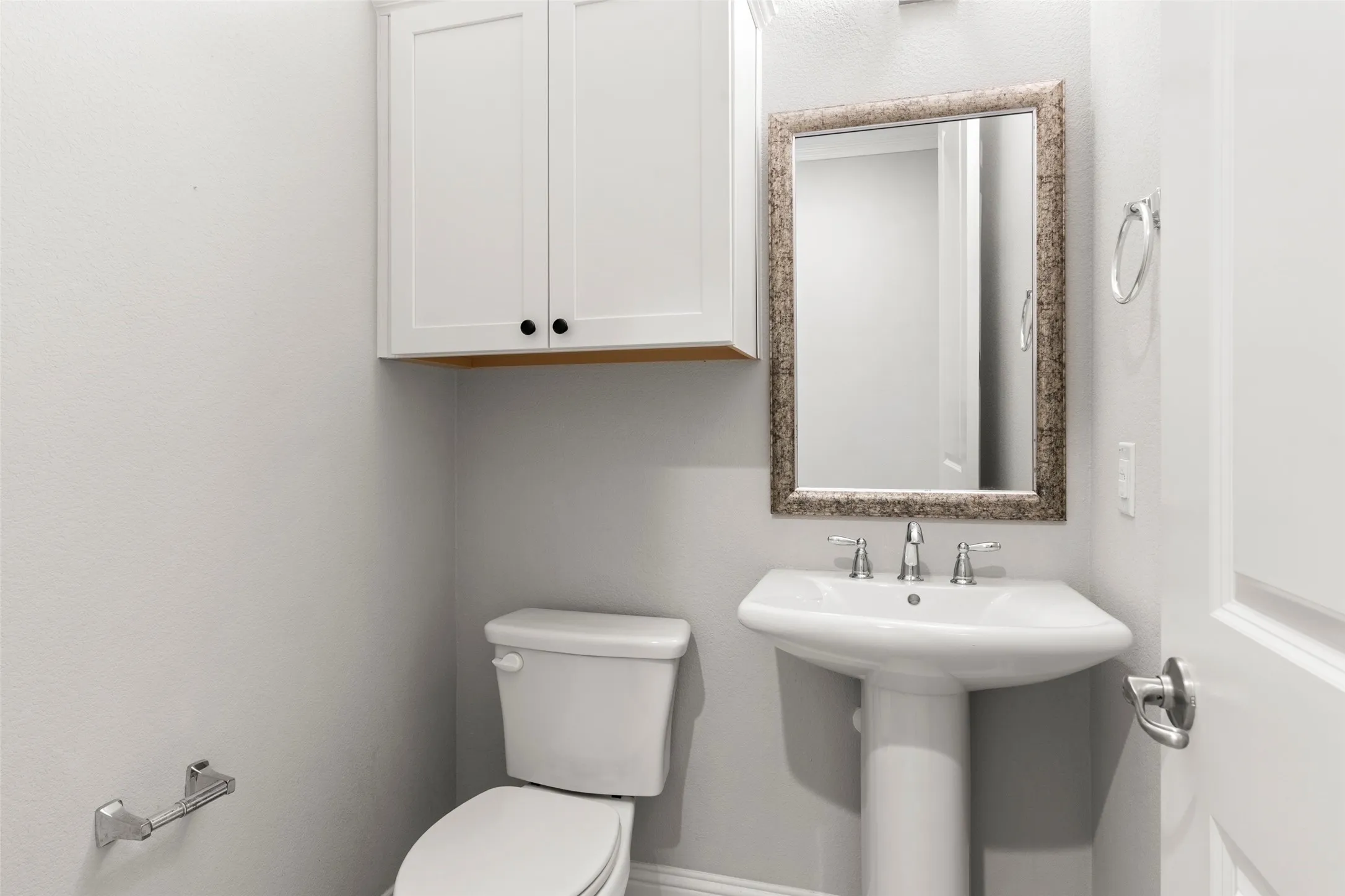 Bright, efficiently designed half bath featuring a pedestal sink with chrome faucet, white porcelain toilet, and framed mirror