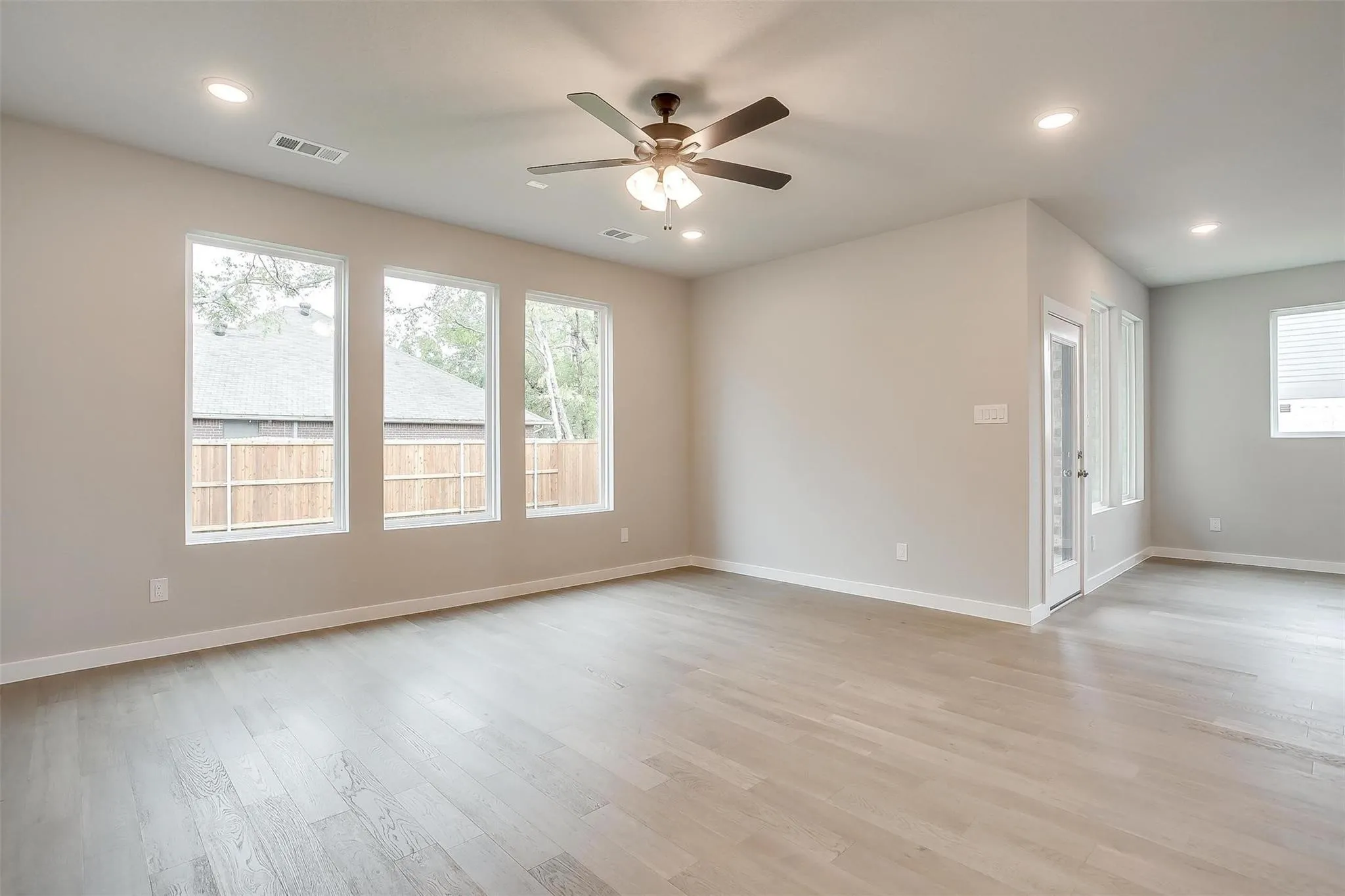 Spacious living area featuring light wood-finish flooring, recessed lighting, a ceiling fan, and multiple large windows