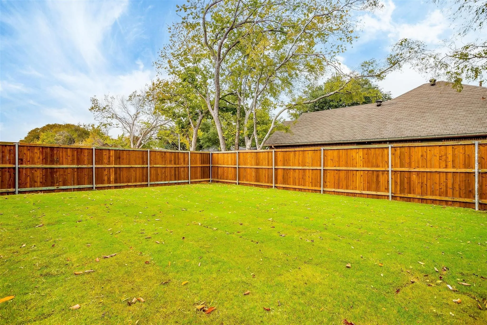 Expansive backyard featuring a manicured lawn, wood fencing, and mature trees