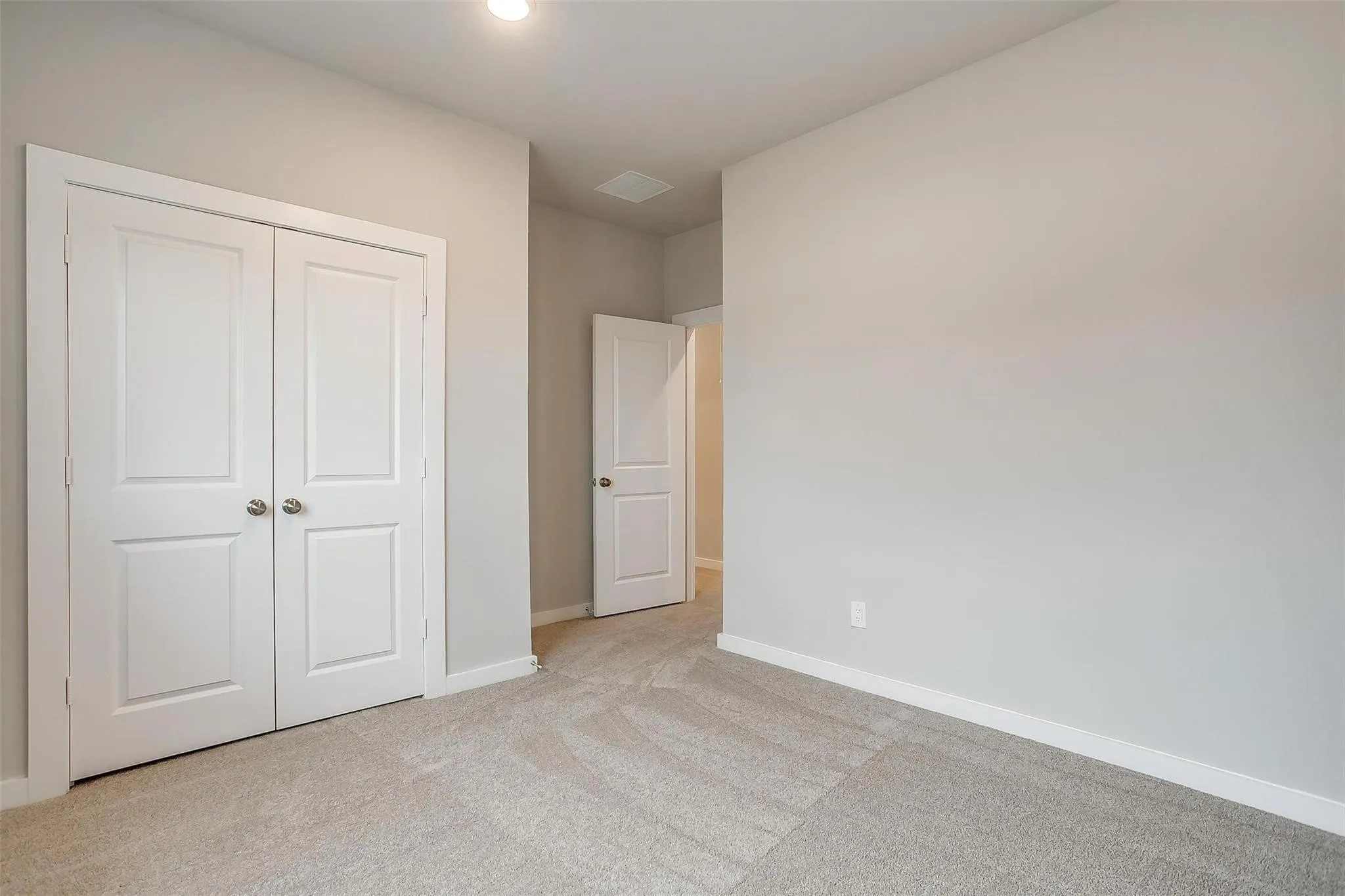 Recessed ceiling lighting, light gray wall paint, off-white trim, gray patterned carpet, and white paneled doors with chrome hardware