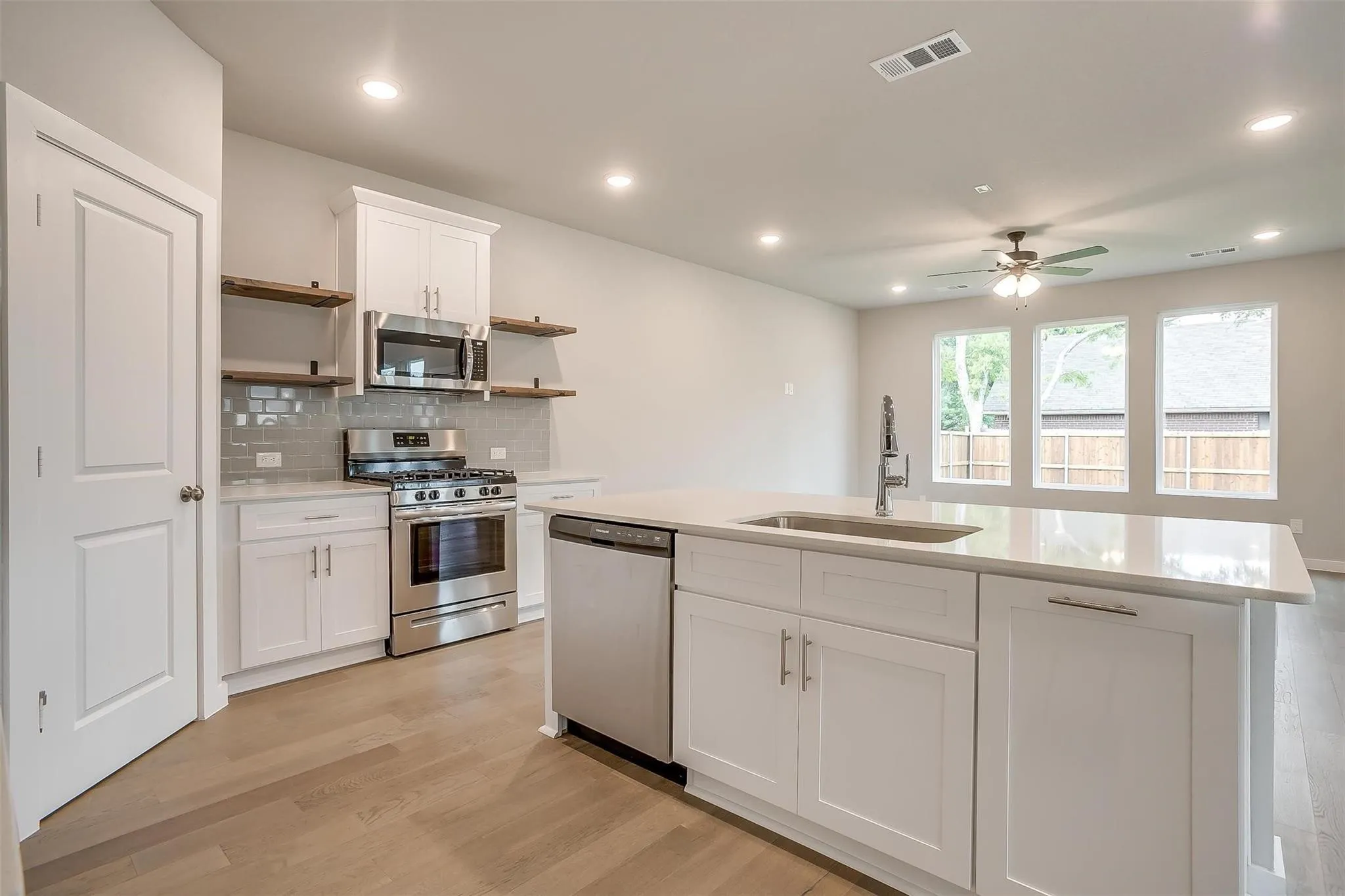 Modern kitchen featuring white cabinetry, stainless steel appliances, a tile backsplash, wood-finish flooring, and a large island with an undermount sink