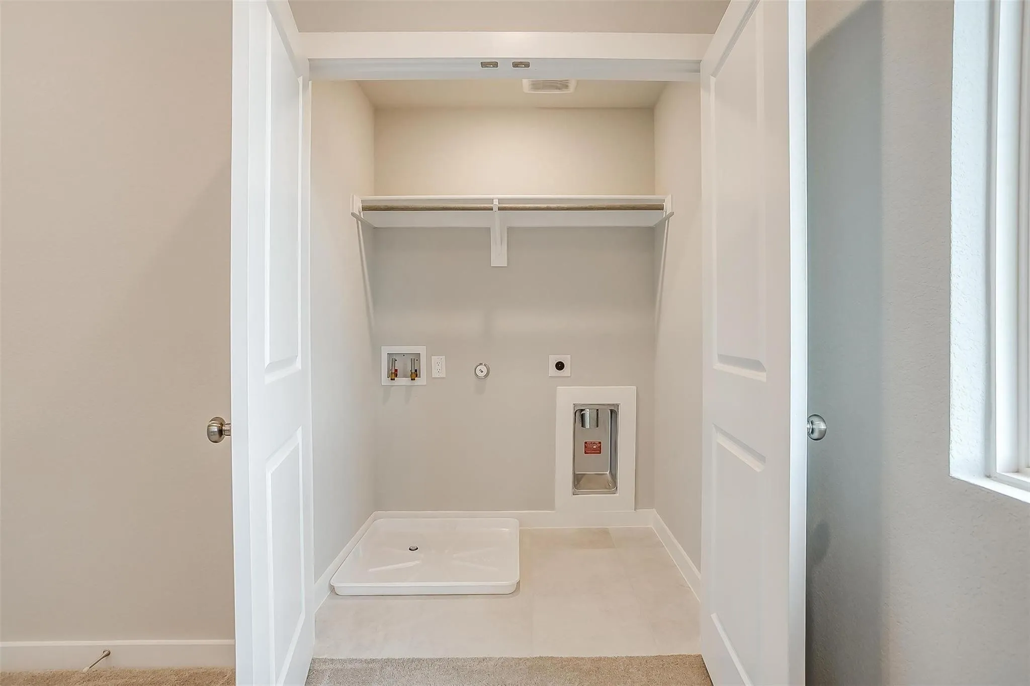 Laundry closet with white bi-fold doors, upper shelving, and a washing machine hookup