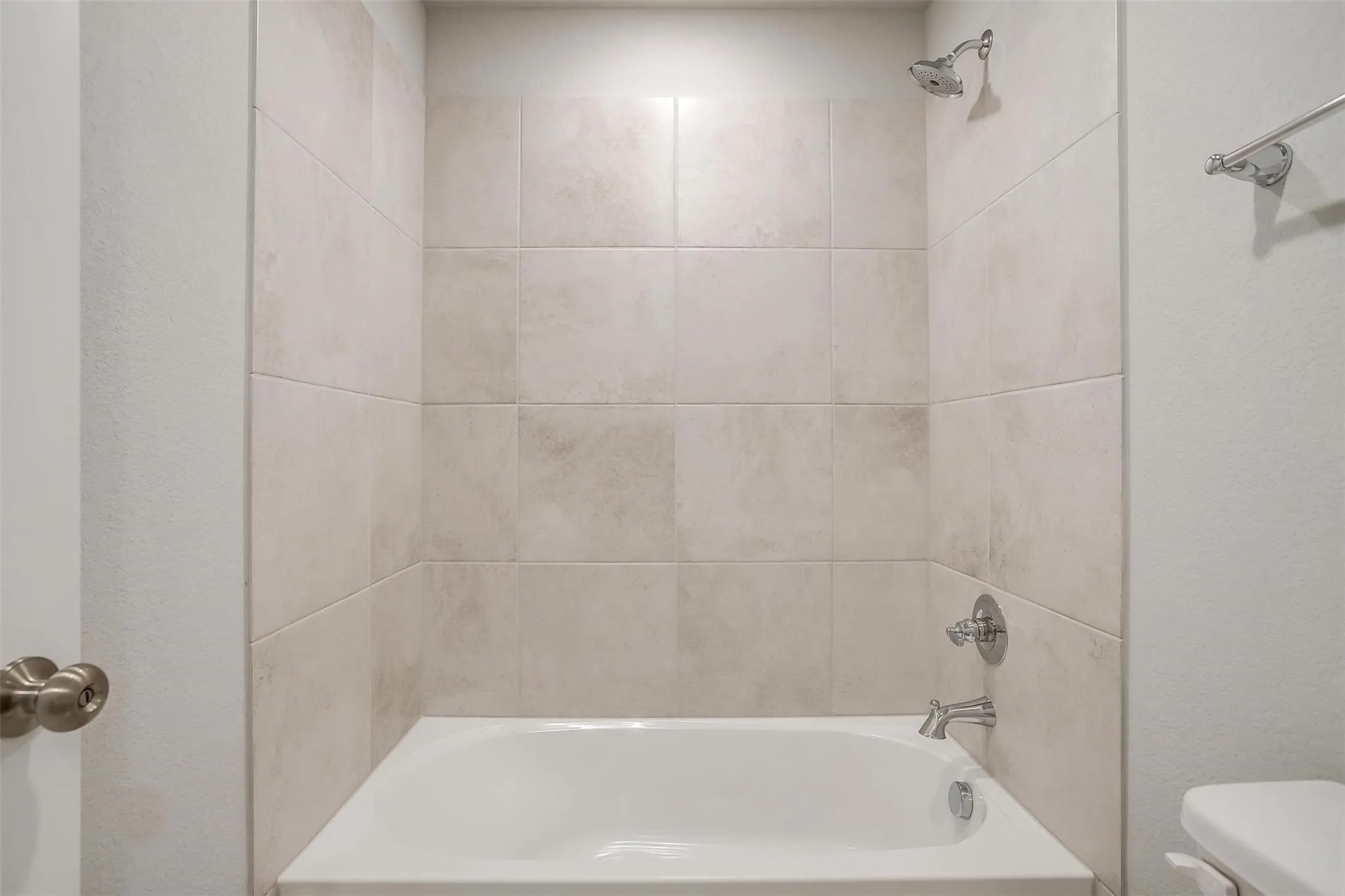 Bathtub with tiled surround, chrome showerhead, and coordinating bath fixtures