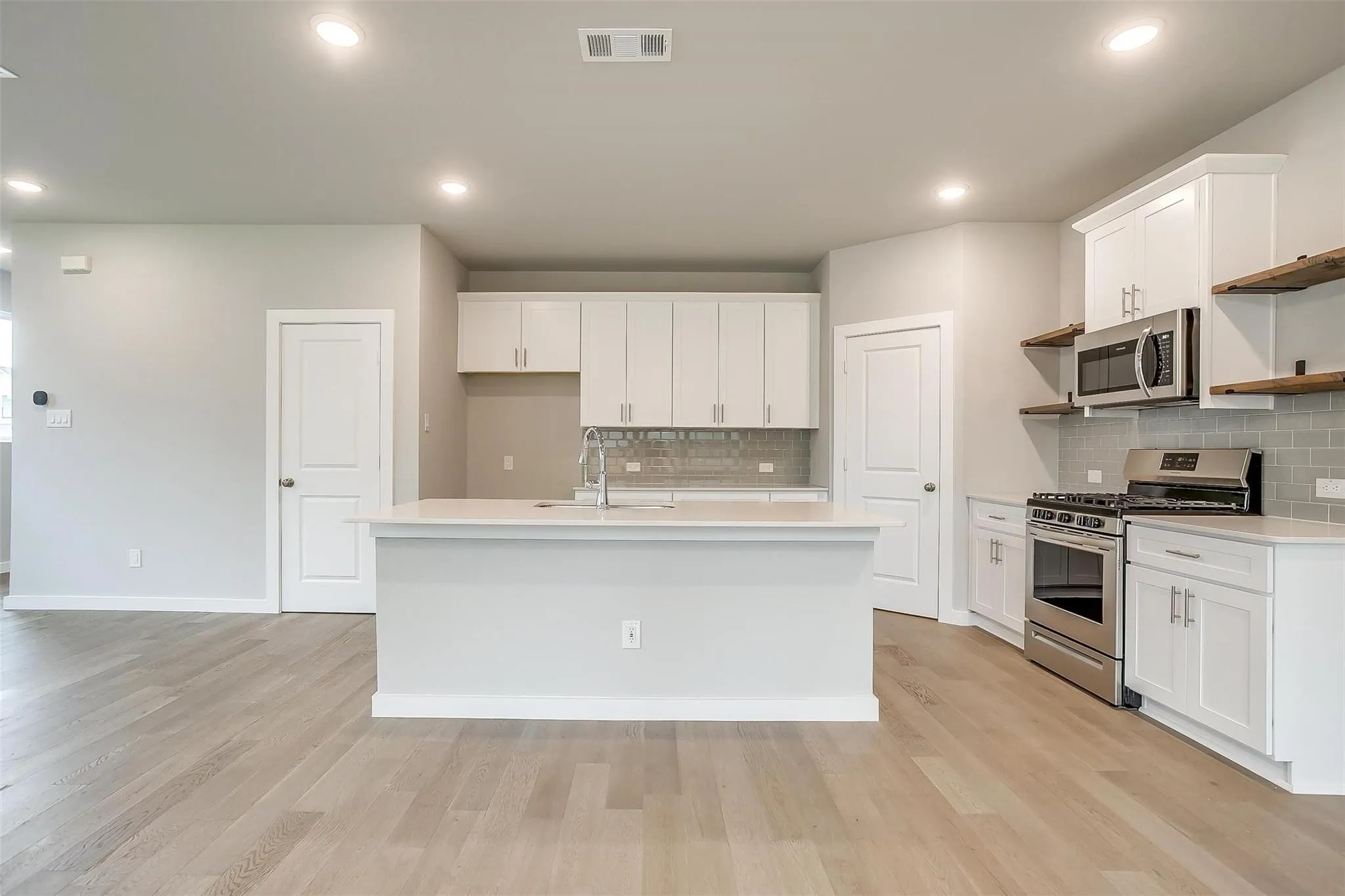 Kitchen featuring an island with a sink, white cabinetry, stainless steel appliances, and wood-finish flooring