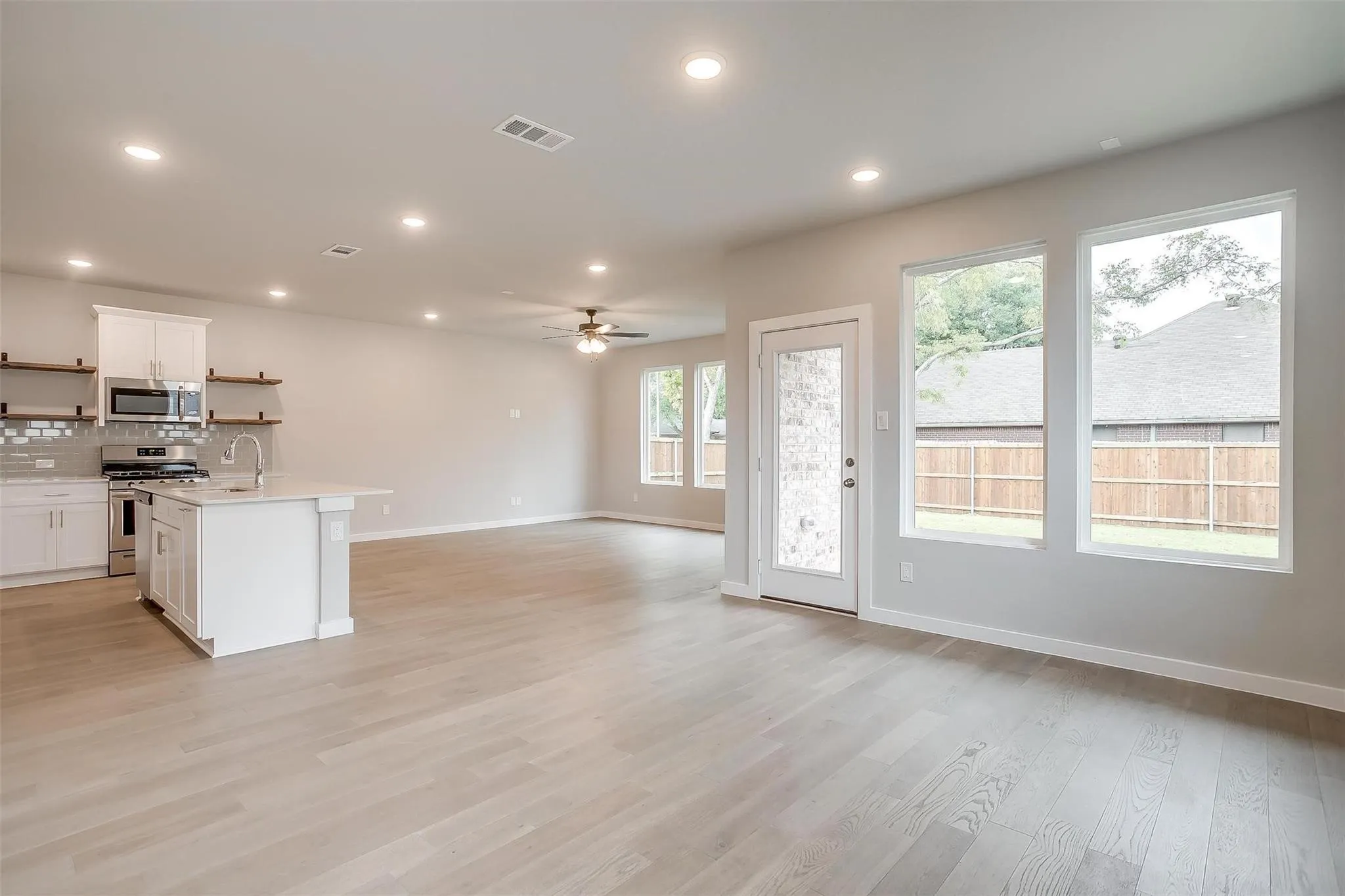 Spacious open-concept living area featuring light wood-finish flooring, recessed lighting, and a ceiling fan