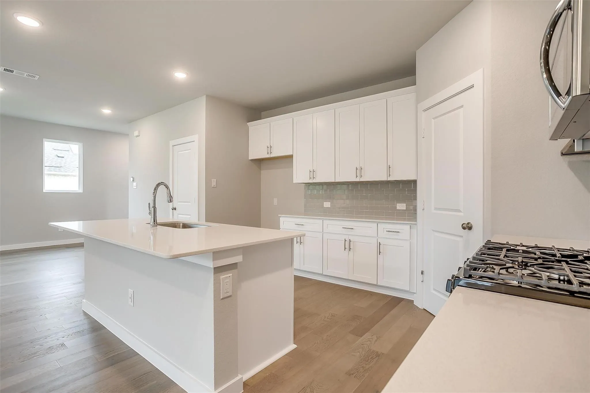 Kitchen featuring a gas range, white cabinetry, a kitchen island with an undermount sink, recessed lighting, and wood-finish flooring