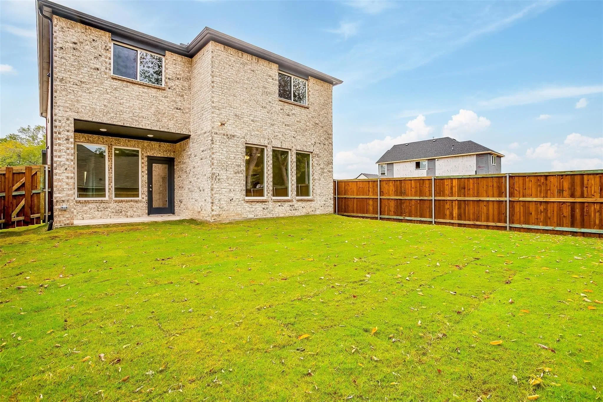 Expansive grassy yard with a wooden privacy fence, a brick exterior, a covered patio, and large windows