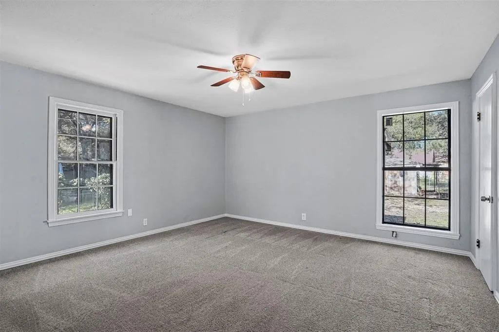 Wall-to-wall carpeting, two large paneled windows, and a ceiling fan with integrated lighting