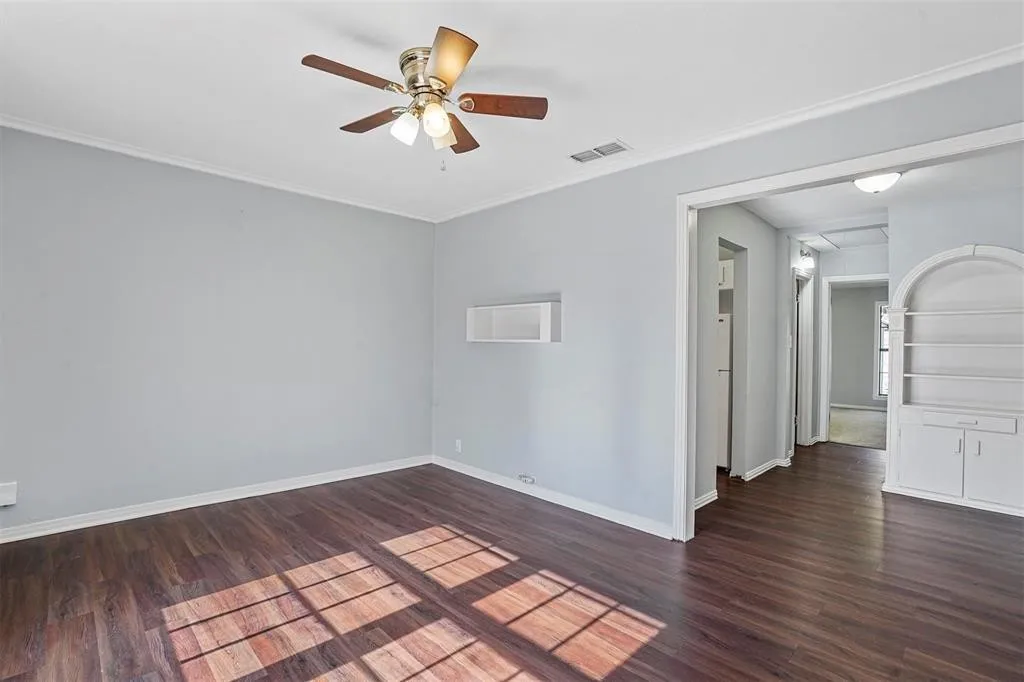 Wood-finish flooring, ceiling fan with integrated lighting, built-in shelving with lower cabinetry, and recessed wall opening
