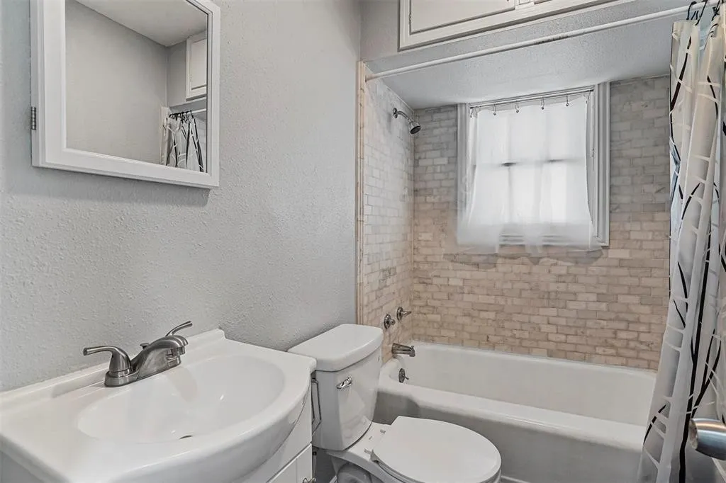Bathroom featuring a white vanity with integrated sink, brushed nickel faucet, wall-mounted mirror, and a bathtub with subway tile surround