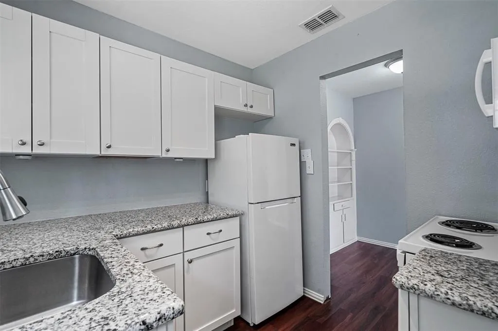 White cabinetry with brushed nickel hardware, speckled countertops, stainless steel sink, and wood-finish flooring