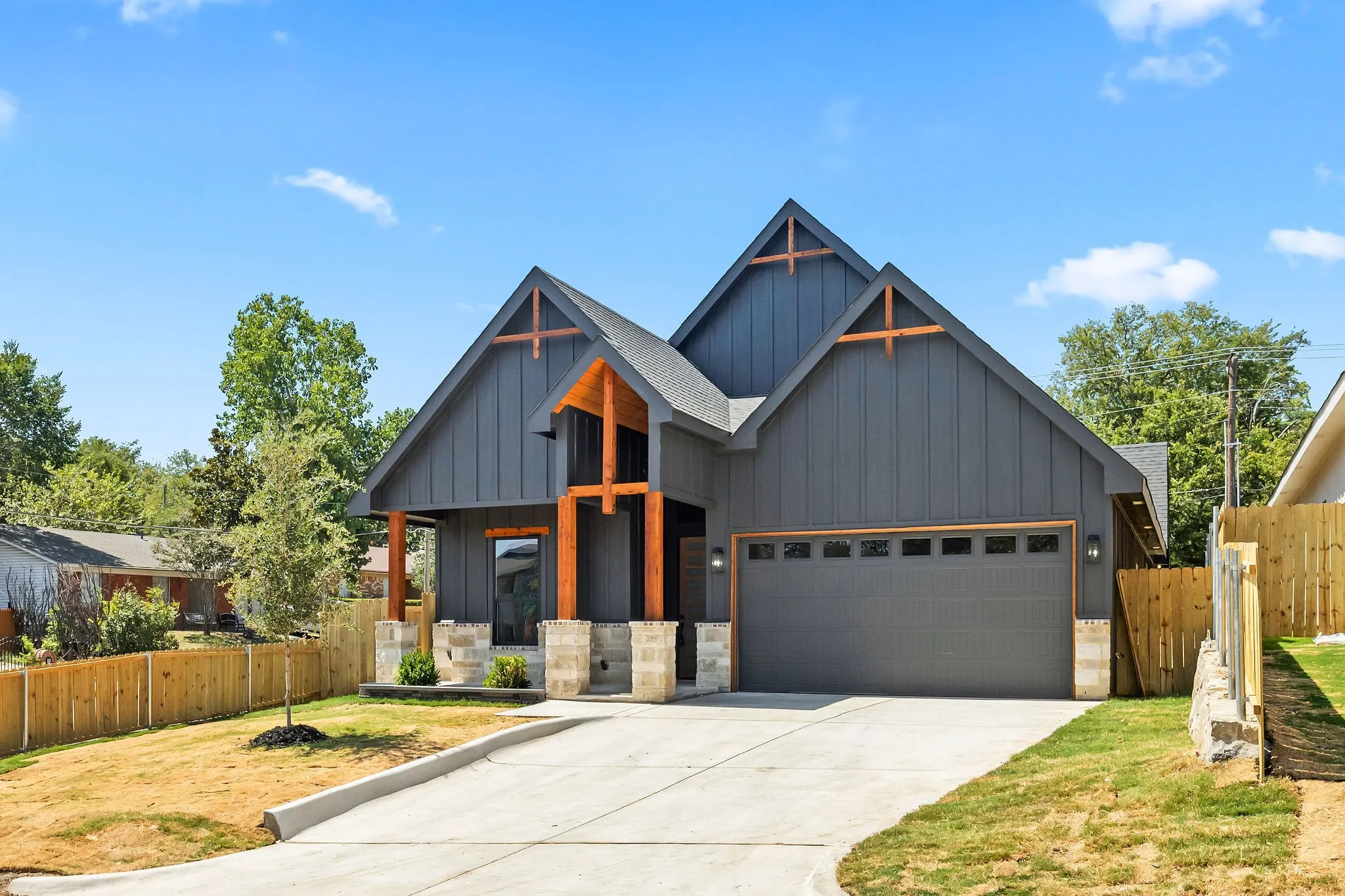 Modern exterior with dark vertical siding, exposed wood beams, and stone pillar accents