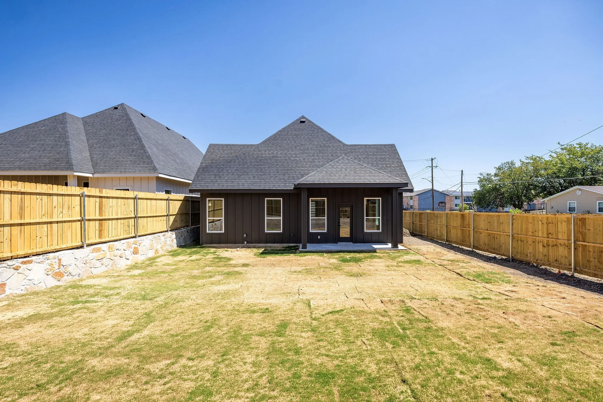 Rear exterior featuring vertical dark siding, multiple windows with white trim, and a dark shingled roof