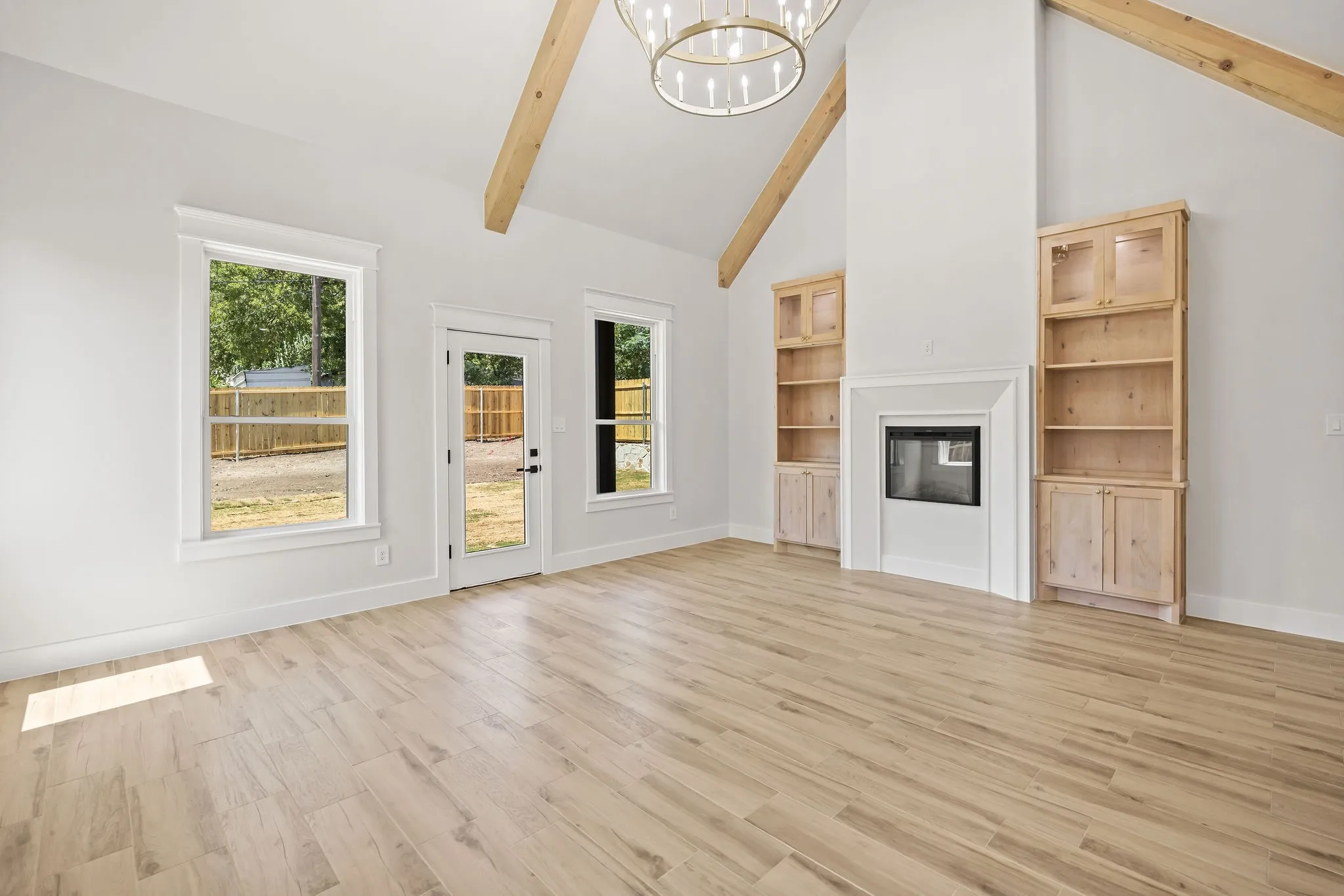 Vaulted ceiling with exposed wood beams, wood-finish flooring, built-in fireplace, and custom built-in cabinetry with glass-front uppers