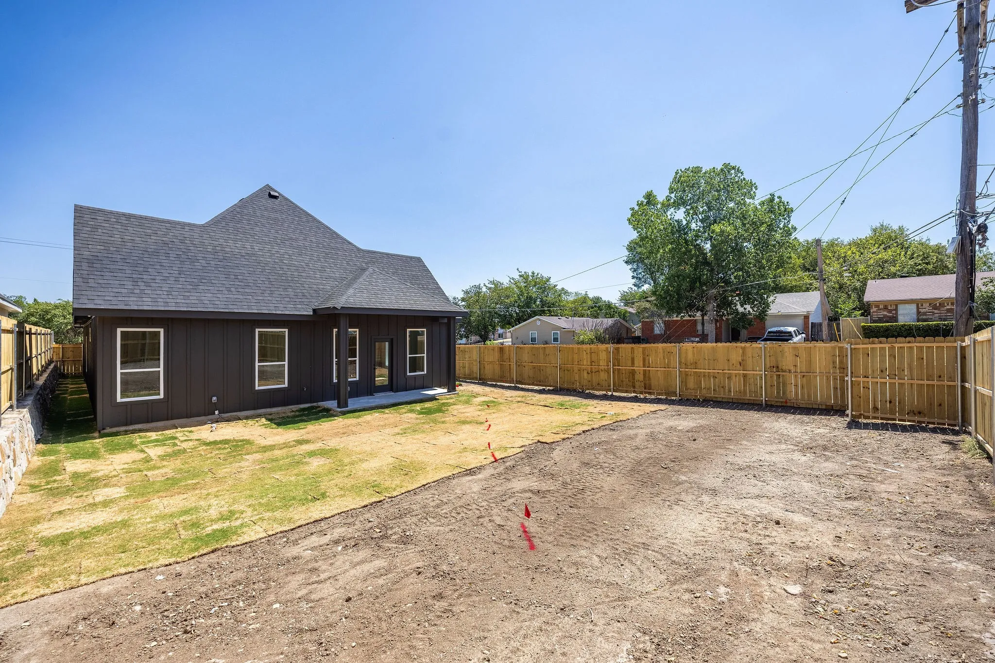 Dark-toned exterior siding with white window frames, covered patio area, dark shingle roof, and a wood privacy fence