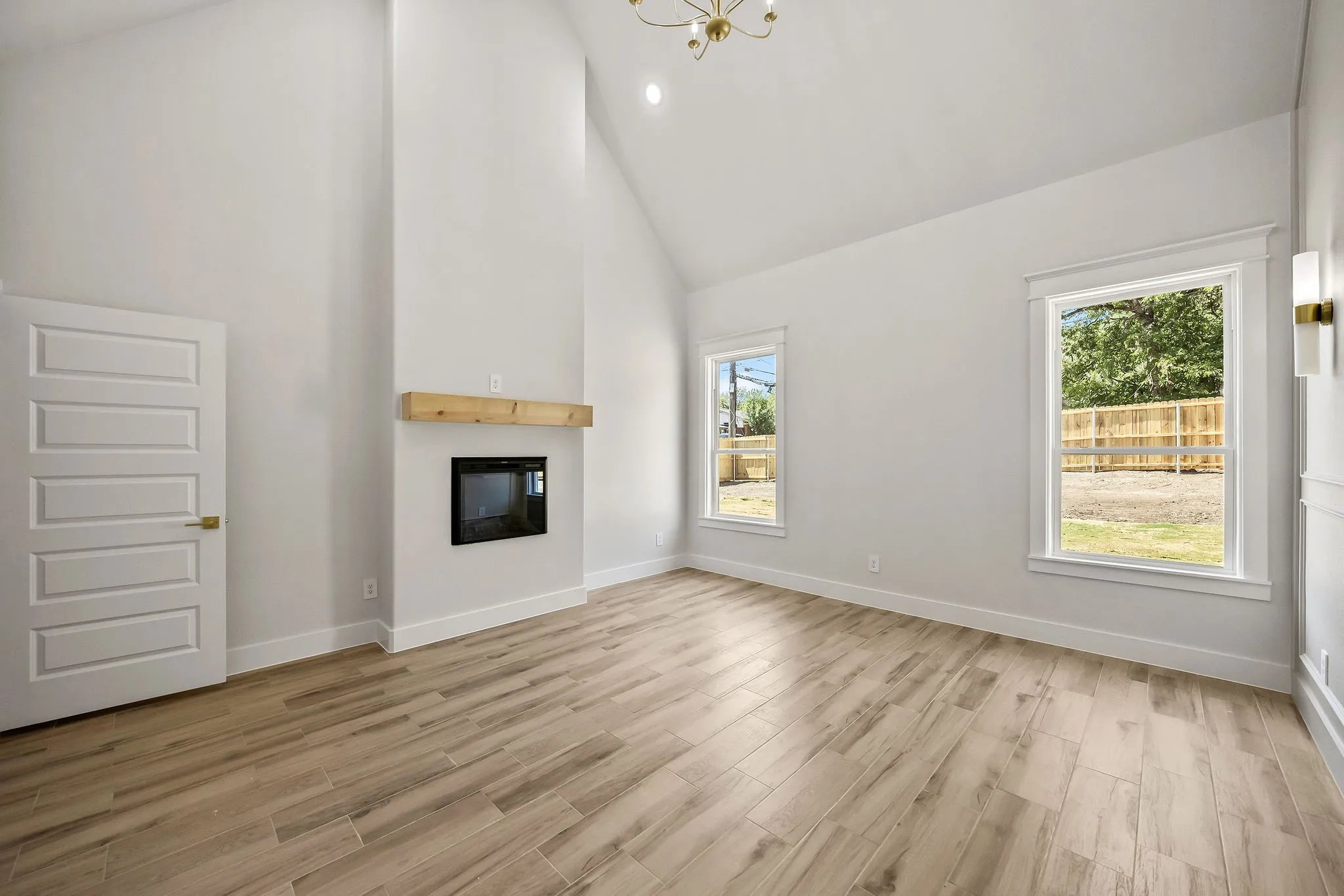 Vaulted ceiling, wood-finish flooring, built-in fireplace with wood mantel, five-panel interior door, and large windows
