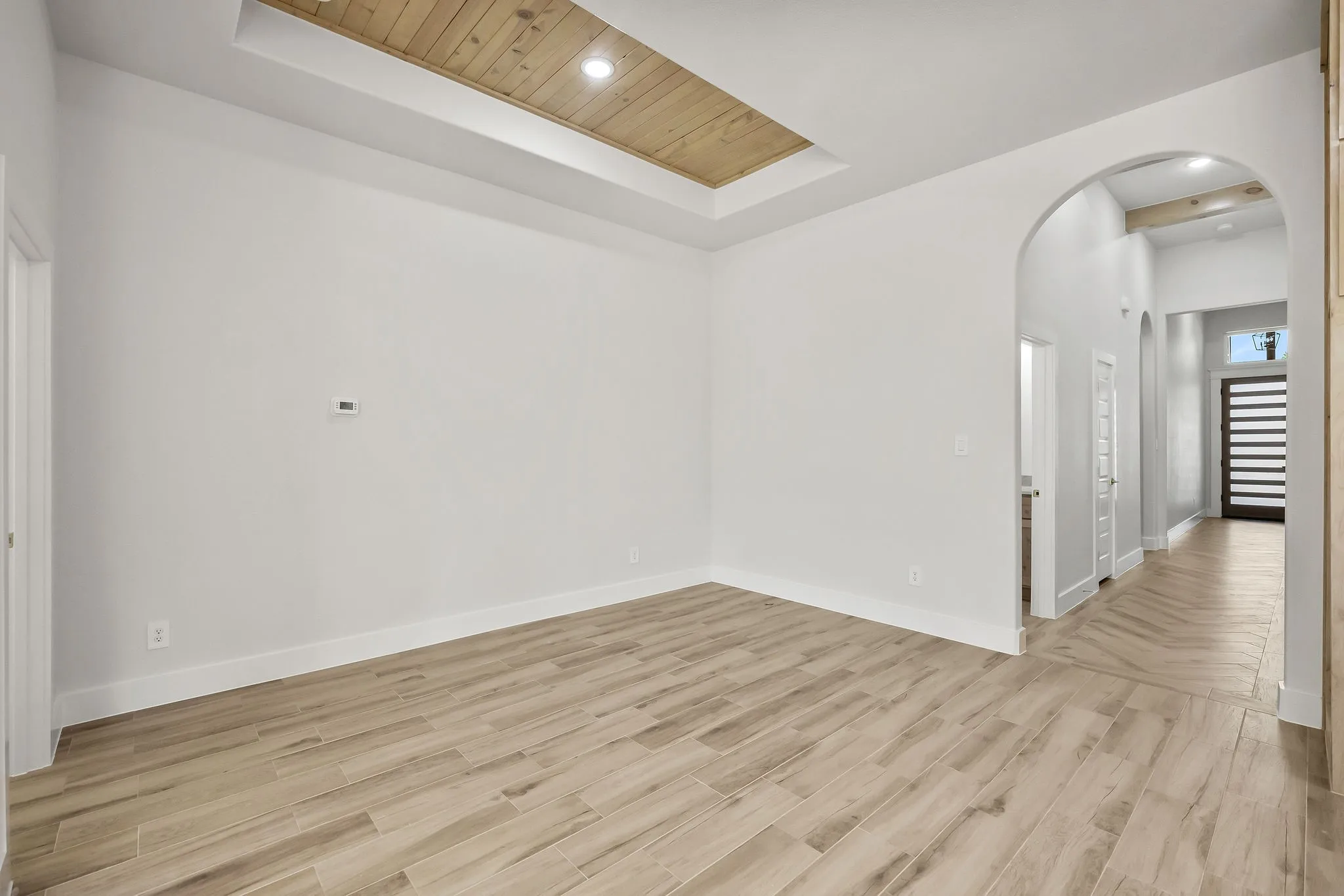 Wood-finish tile flooring throughout, tray ceiling with wood paneling, recessed lighting, and arched doorways