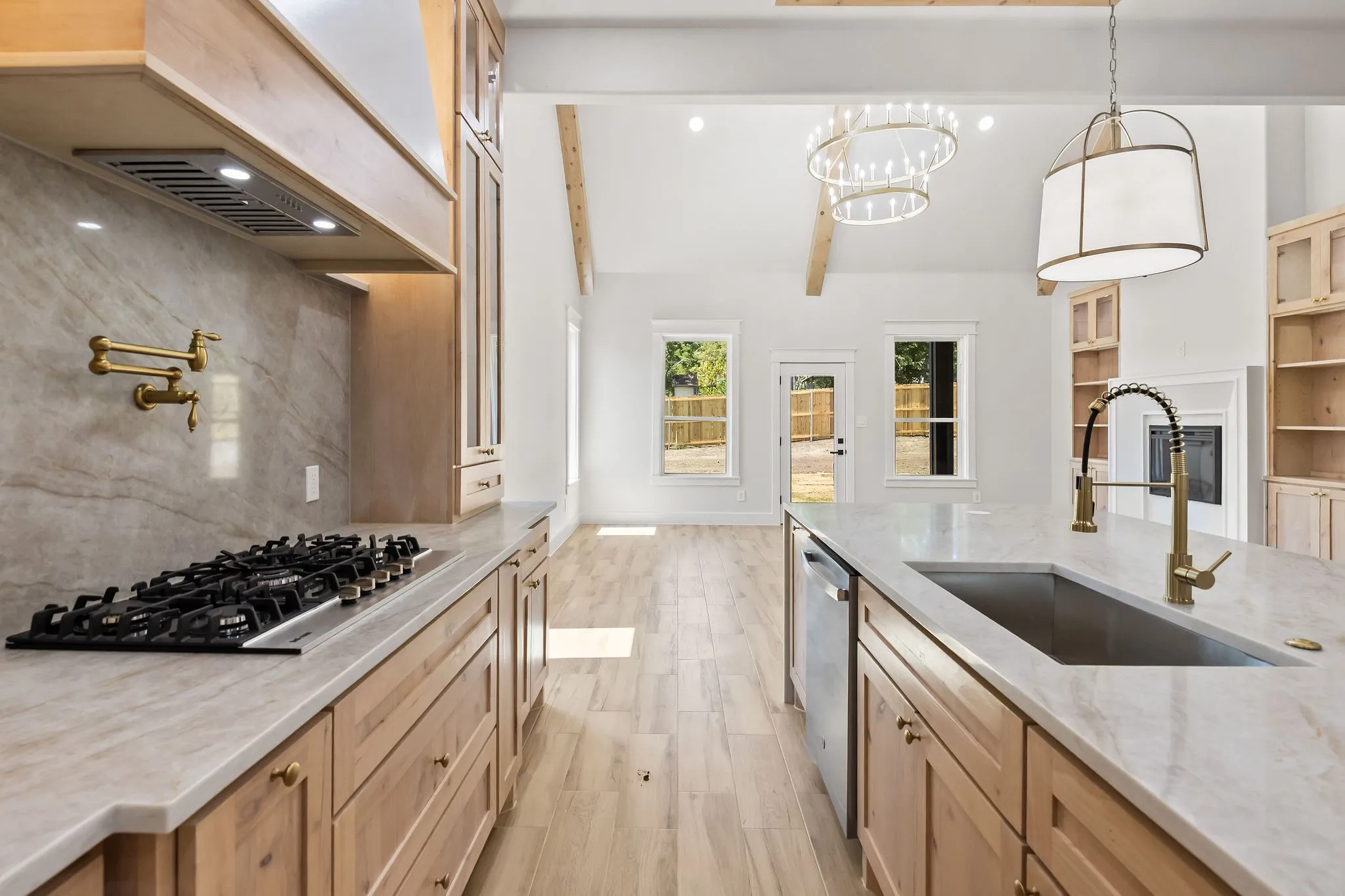 Kitchen featuring a gas range, pot filler, kitchen island with an undermount sink, and light wood-finish cabinetry