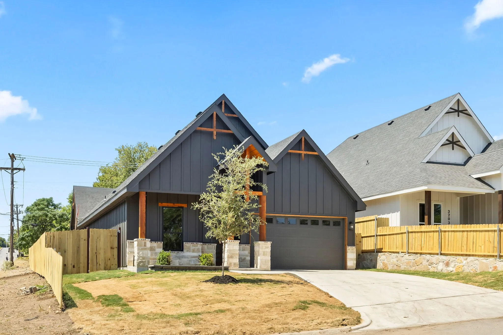 Modern farmhouse exterior with dark vertical siding, stone accents, attached garage, and a wood privacy fence