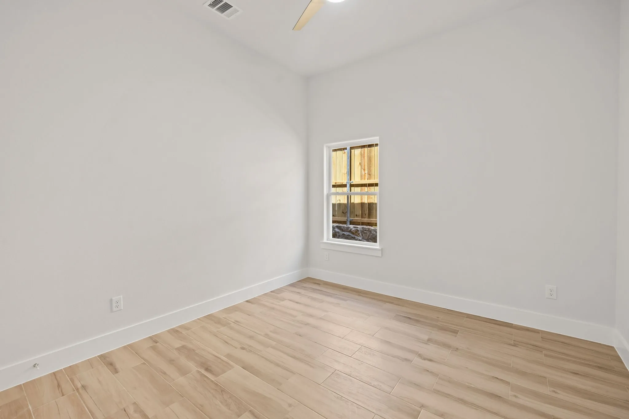 Wood-finish flooring, single window, crisp white walls, and a ceiling fan